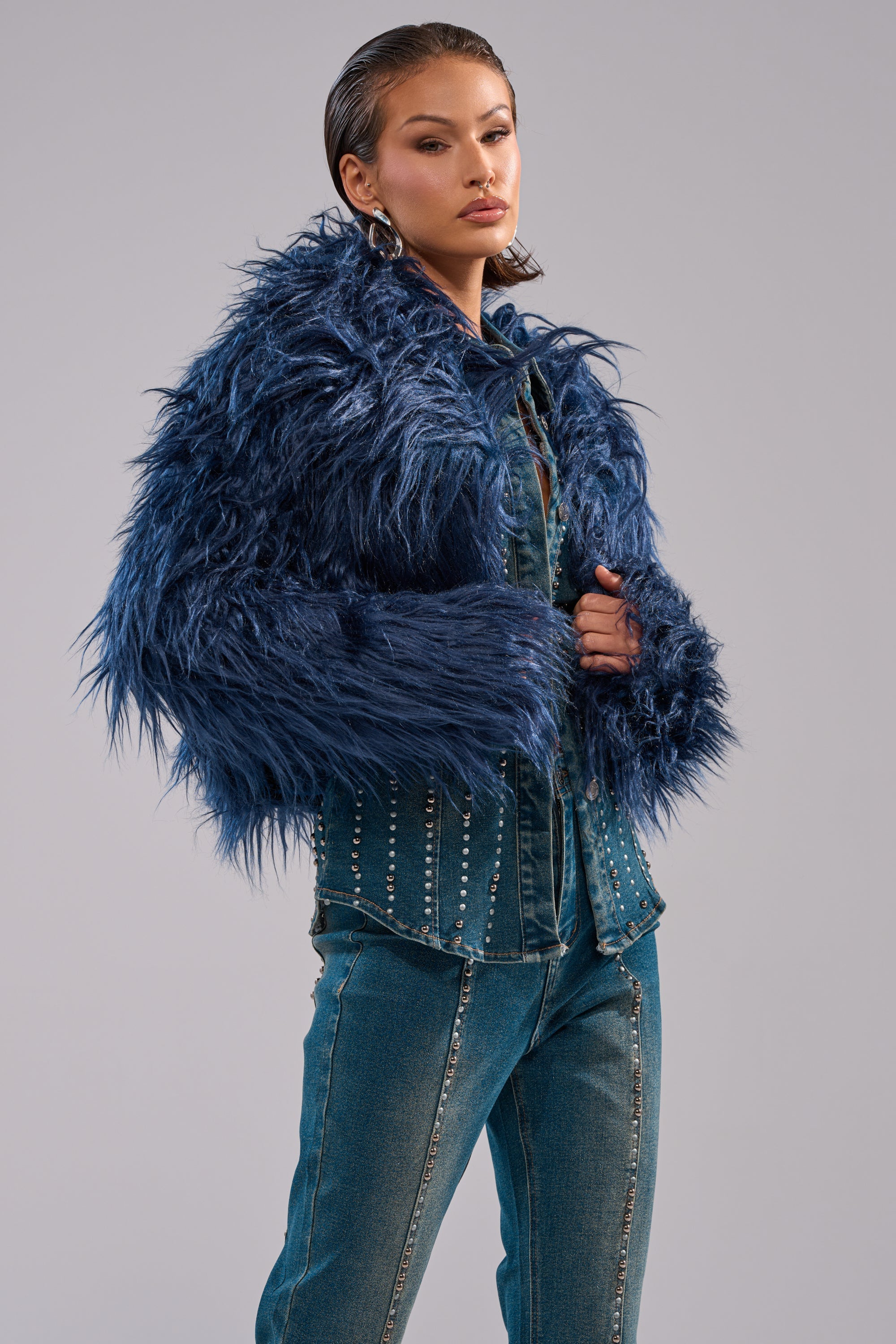 A person wears the LIFE OF THE PARTY FAUX FUR jacket over a studded denim shirt and blue jeans, standing against a plain light gray background. 1