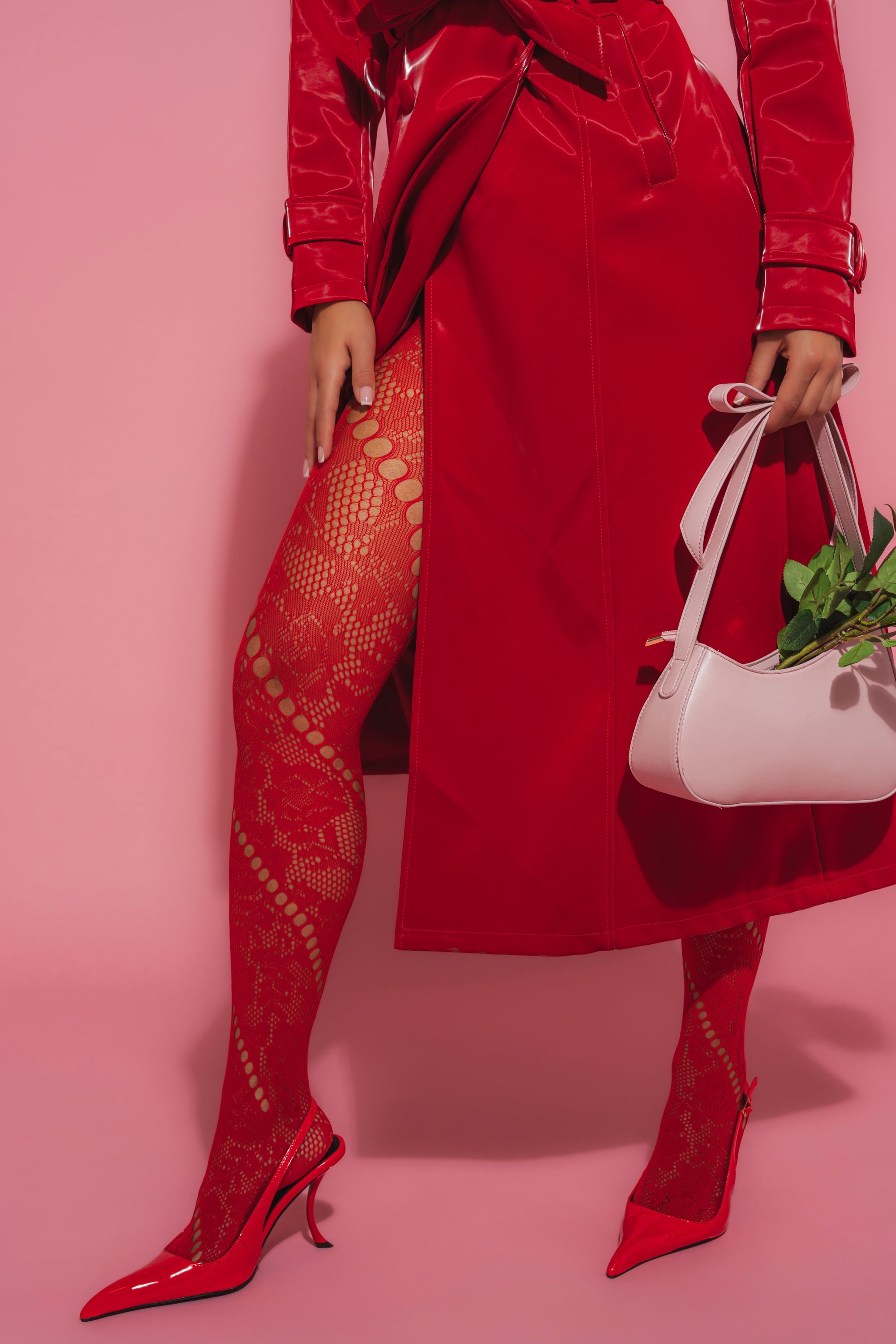 Wearing LACED FEELINGS TIGHTS, a red trench coat, and red heels, a person stands against a pink background holding a pale pink handbag with green leaves inside. 0