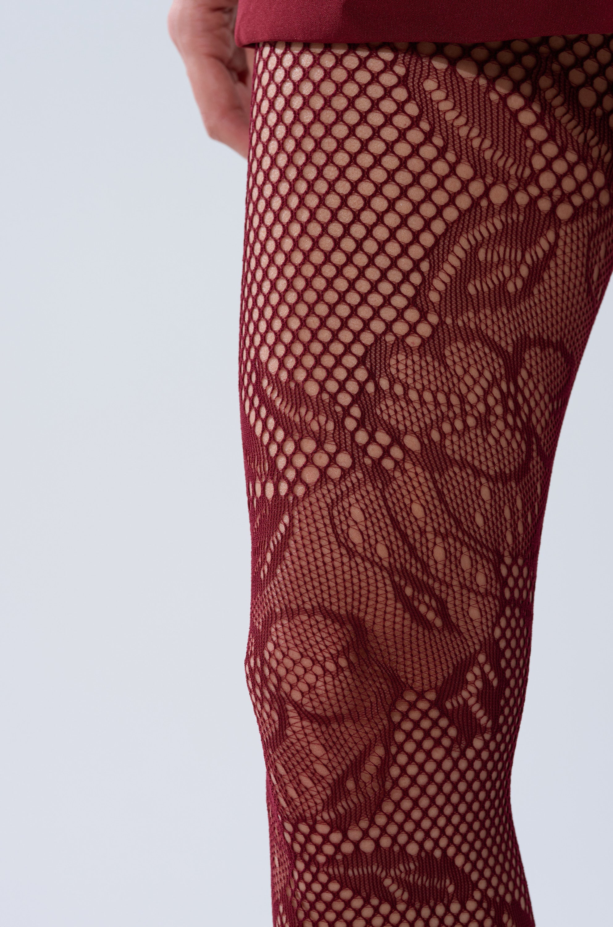A close-up shows a person's leg wearing the REALLY WITH IT LACE TIGHTS IN BURGUNDY, featuring a floral lace pattern against a plain, light-colored background. 2