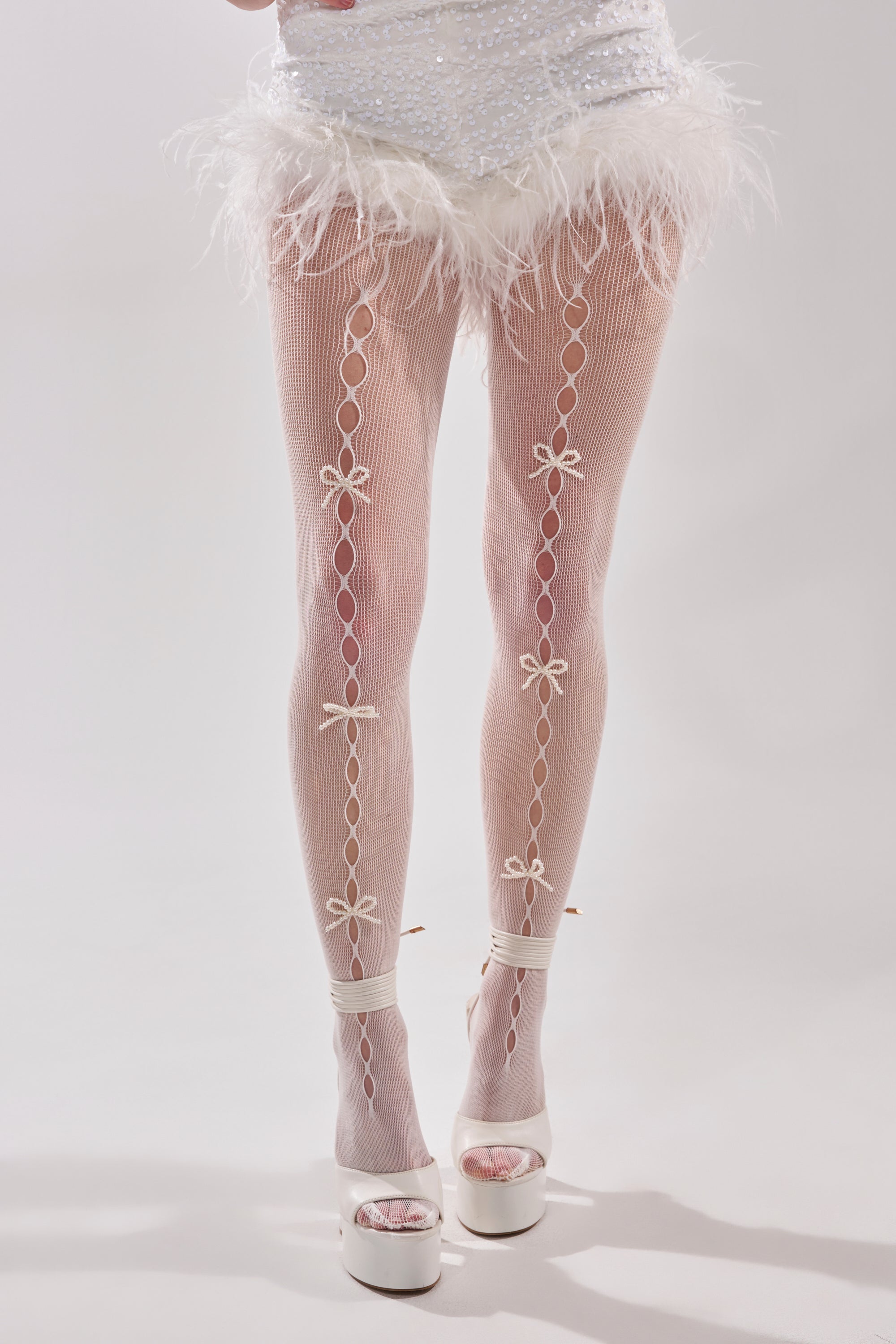 Wearing ANGEL SEASON TIGHTS with white textured feather-trim shorts and white high platform heels, the person stands against a plain light background. 0