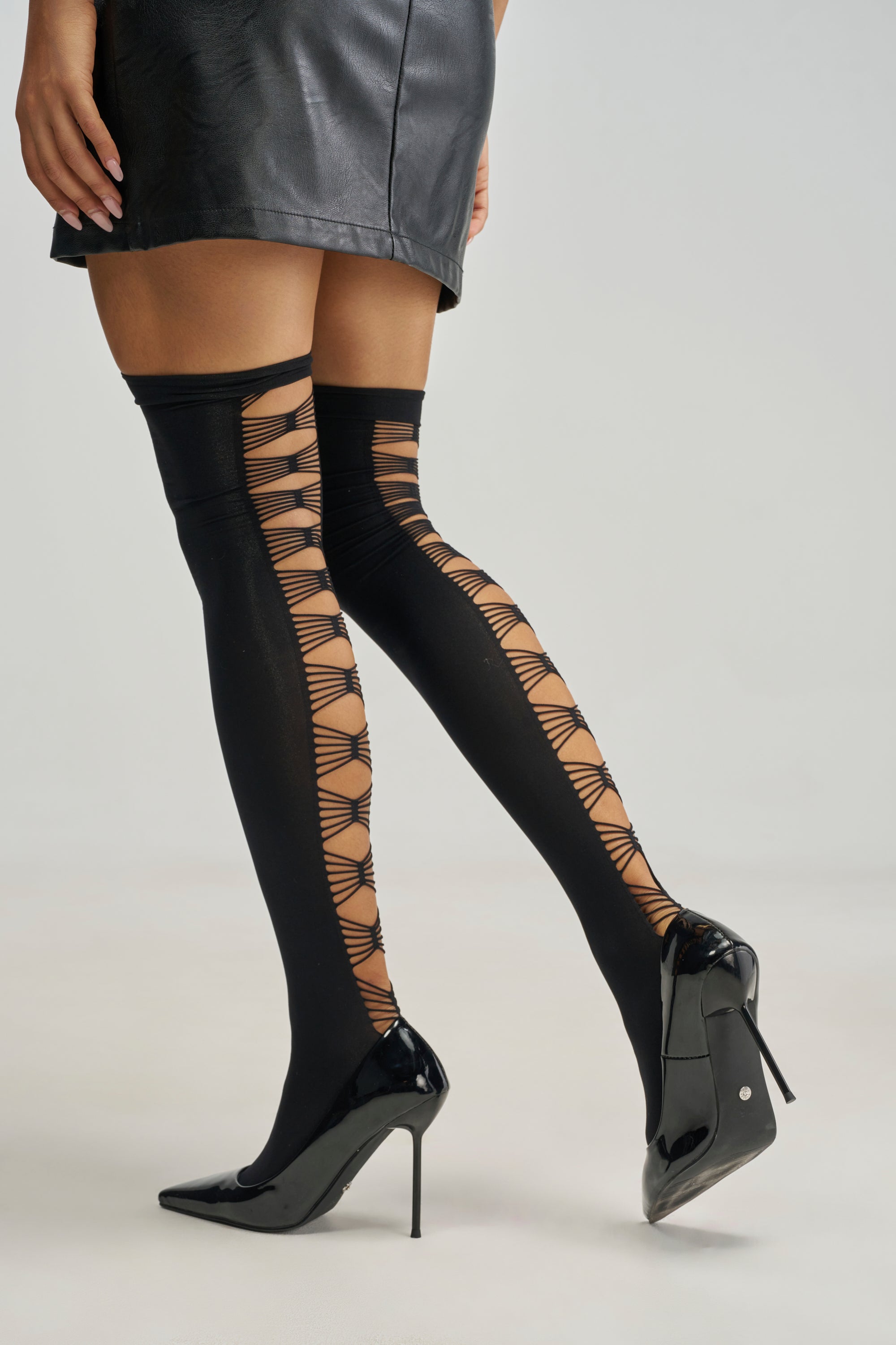 PRETTY LADY TIGHTS in black featuring a vertical ladder-style cutout design down the back of the legs, worn with black pointed-toe high heels and a short skirt.