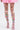 A person stands against a plain light background wearing ITS POPPIN EMBELLISHED TIGHTS—white tights with colorful floral embellishments—paired with a pink skirt and pink lace-up sandals.