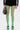 A person wearing GREEN WITH NO ENVY TIGHTS, a black high-rise ruffled skirt, a black jacket with white sleeve stripes, silver-embellished black shoes, and holding a small black handbag with colorful accents.
