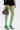 Wearing GREEN WITH NO ENVY TIGHTS, black high-heeled sandals with silver accents, a high-rise ruffled black skirt, and carrying a black handbag with colorful cross-shaped designs.