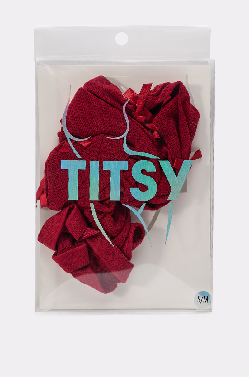 A clear plastic package labeled "IM THE GIFT BOW TIGHTS" holds red, lacy tights for a Holiday Look, featuring a teal outline of a woman's body on the front and a small S/M sticker in the bottom right corner. 5