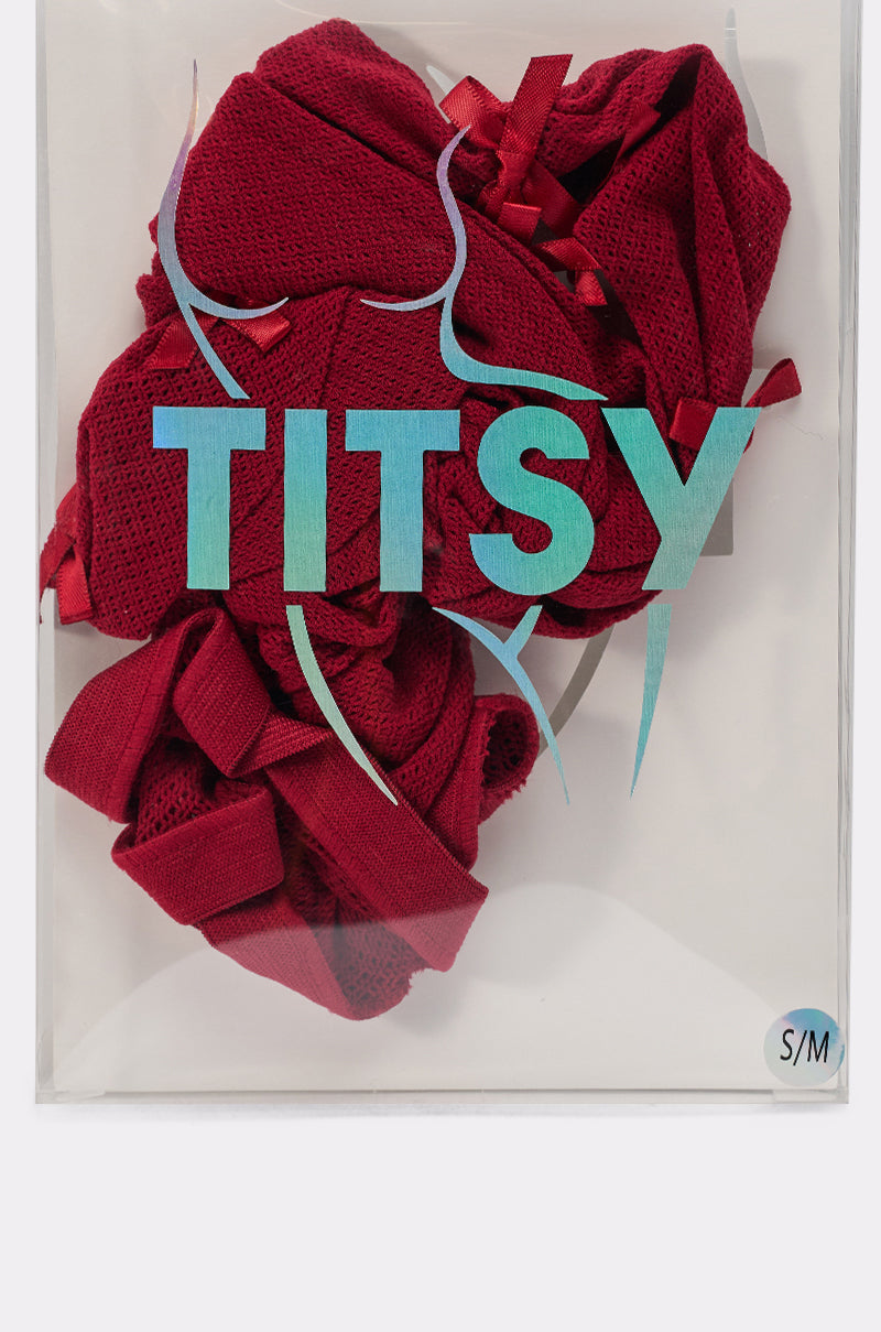 A red "IM THE GIFT BOW TIGHTS" garment is folded behind clear packaging labeled "TITSY" in bold blue letters with a curvy silhouette outline. A small "S/M" size sticker is in the lower right corner. 6