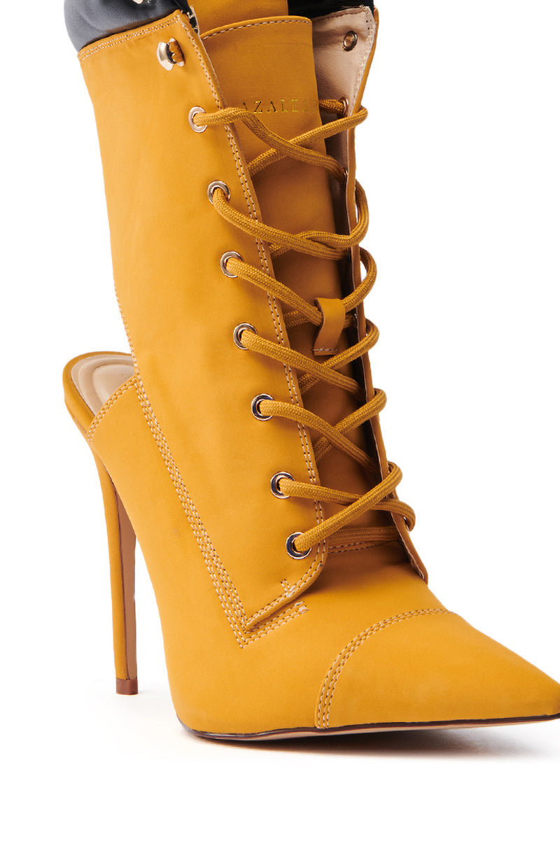 The AZALEA WANG XIOMARA YELLOW LACE UP STILETTO BOOTIE is a mustard yellow, vegan leather boot with a pointed toe, lace-up panel, and cut-out back. It features a unique hybrid design combining elements of stilettos and classic boots.