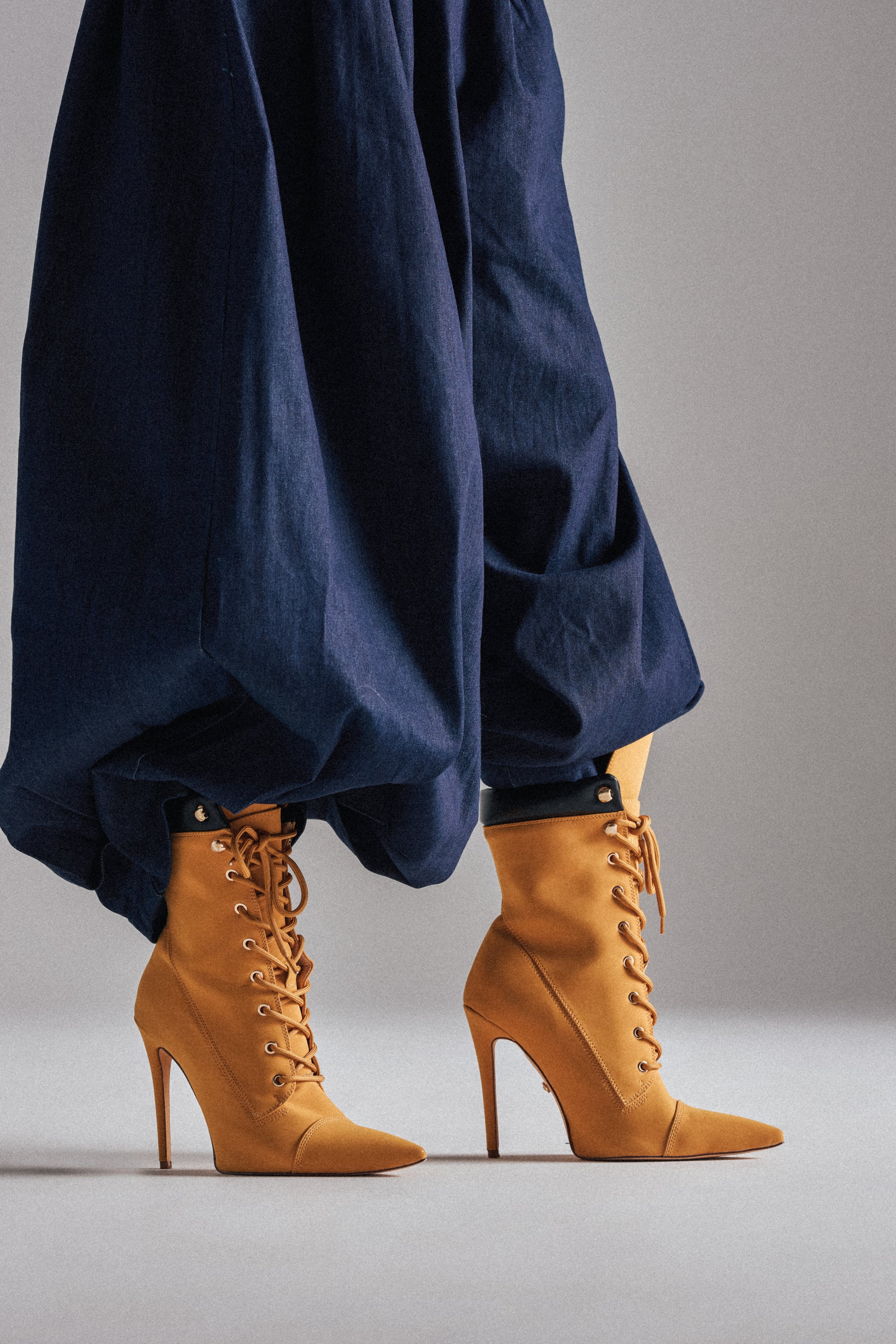 A model wears loose, navy blue pants with the AZALEA WANG XIOMARAN YELLOW BOOTIE stiletto heel boots, standing against a plain gray background.
