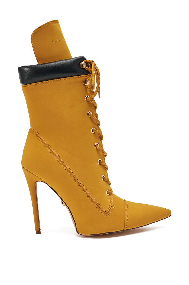 The AZALEA WANG XIOMARAN YELLOW BOOTIE is a mustard faux suede bootie with a pointed toe, lace-up front, black folded-over top edge, silver eyelets, and an elegant stiletto heel for a bold statement.