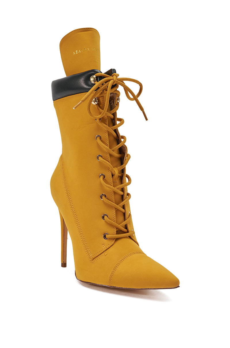 The AZALEA WANG XIOMARAN YELLOW BOOTIE is a mustard yellow faux suede bootie with a pointed toe, black padded collar, and stiletto heel, shown against a white background.