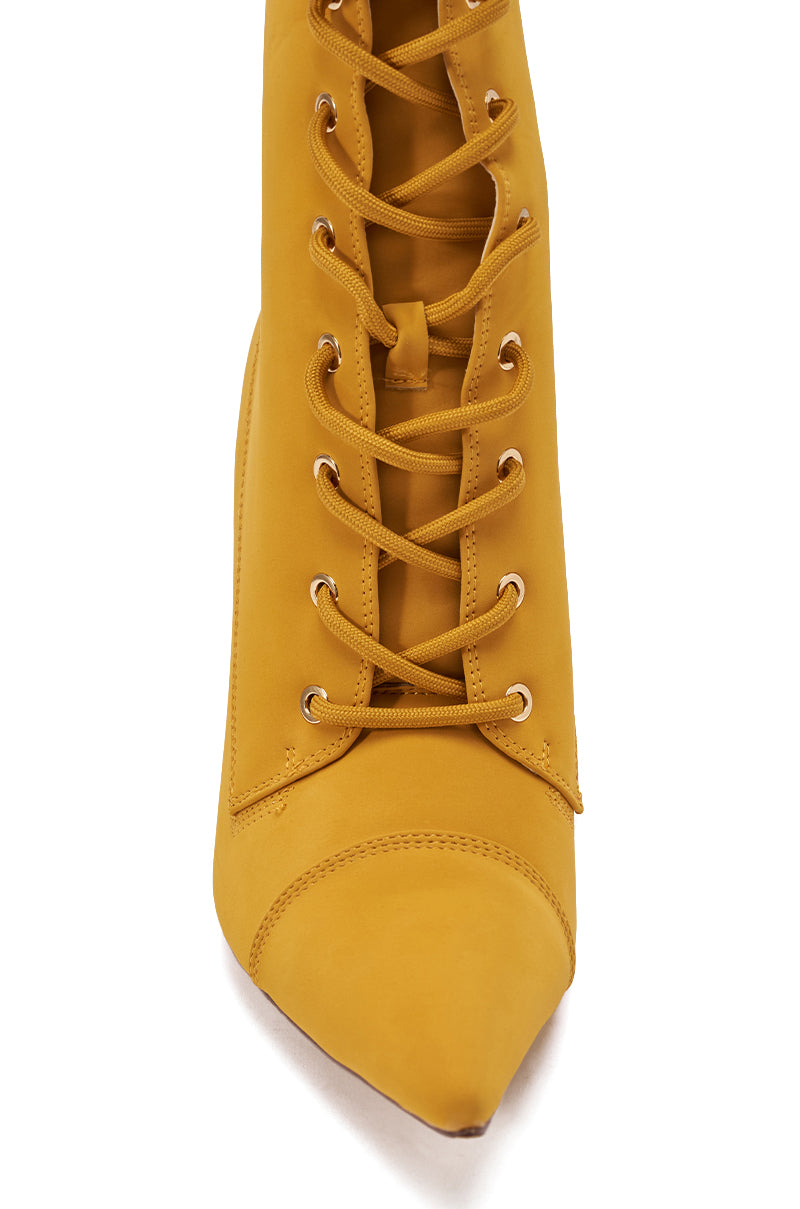 The AZALEA WANG XIOMARAN YELLOW BOOTIE features a pointed toe, faux suede finish, gold eyelets, crisscross lace-up front, and detailed stitching on the toe cap, as seen from above.