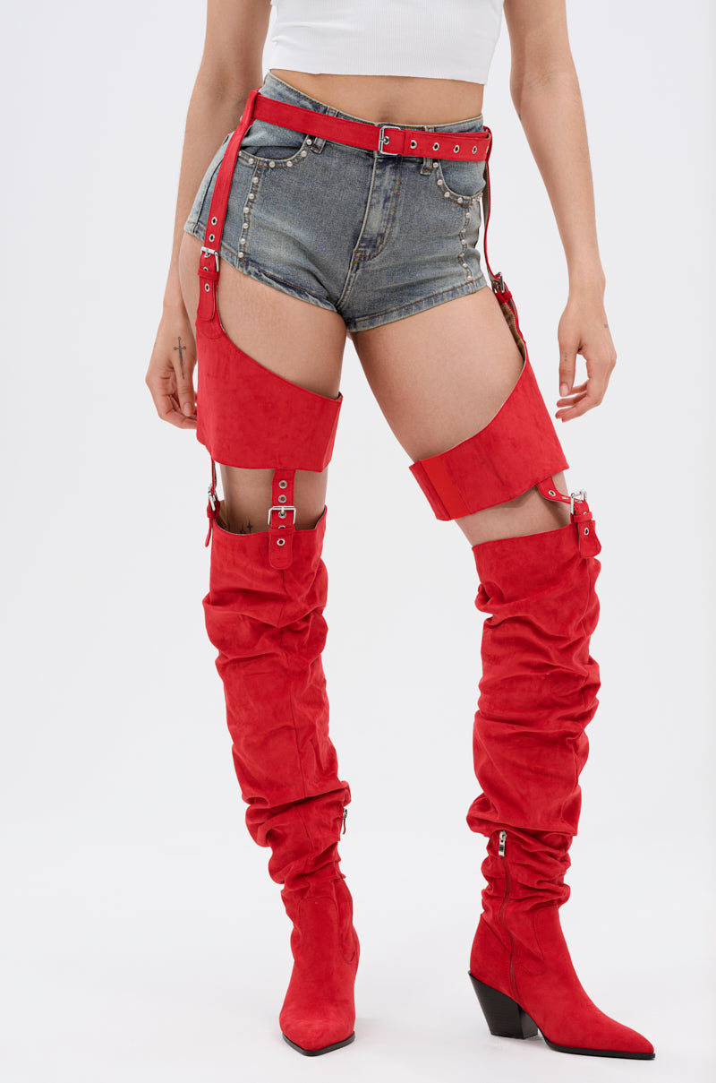 A person wears a white crop top, denim shorts, and AZALEA WANG XOMARIA Red Faux Suede Western Chap Boots with pointed toes, chunky heels, straps, and belts. The person’s face is not visible. 0