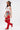 A woman stands confidently in a cowboy hat, white tank top with a red star, denim shorts, and AZALEA WANG XOMARIA RED FAUX SUEDE WESTERN CHAP BOOT against a plain white background.