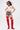 A woman poses confidently in a white crop top with red star pasties, high-waisted denim shorts, the AZALEA WANG XOMARIA RED FAUX SUEDE WESTERN CHAP BOOT, and a black, yellow, and red cowboy hat.