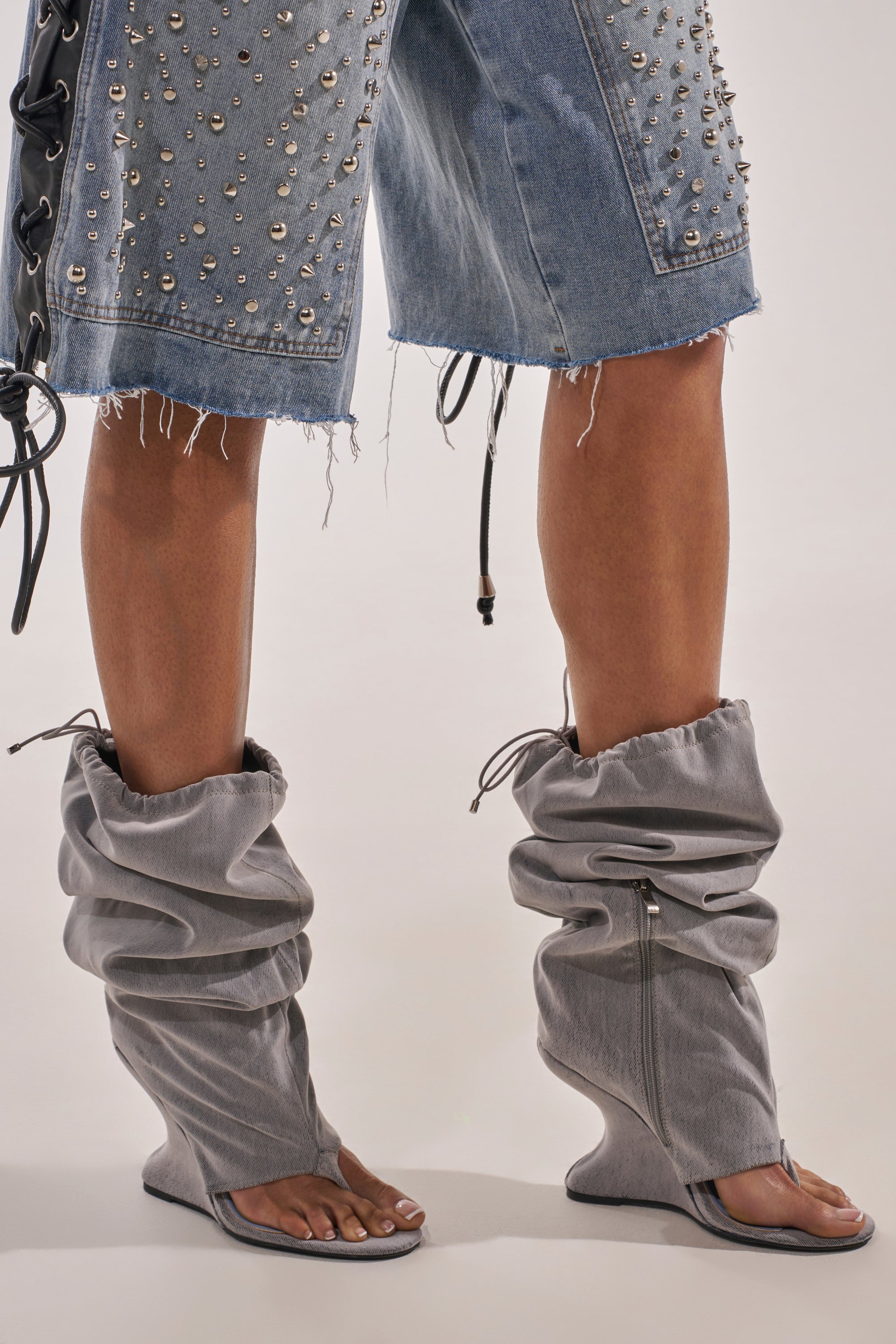 Wearing frayed studded denim shorts and AZALEA WANG XYLAH GREY WEDGE GLADIATOR SANDALS with open toes and heels, exposed legs and feet. The sandals feature zippers and drawstrings for a bold statement look. 1