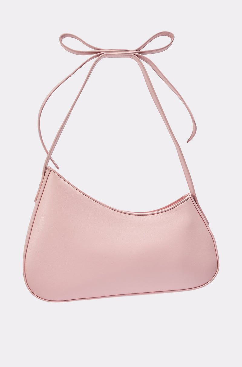 The LOVE YOU LIKE A LOVE SONG PURSE is a minimalist, light pink faux leather handbag with a crescent silhouette and a thin strap tied in a bow, set against a white background. 3