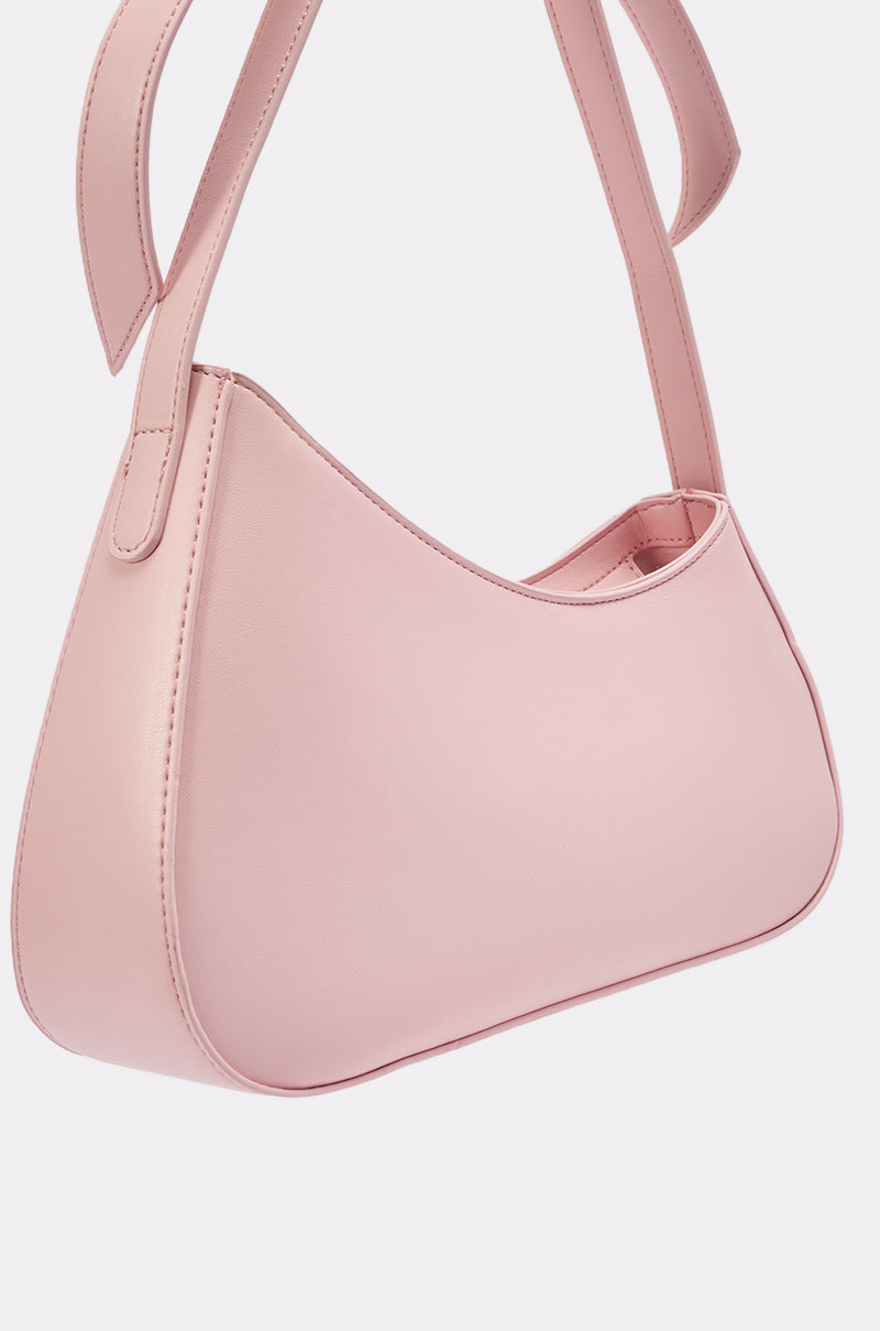 The LOVE YOU LIKE A LOVE SONG PURSE is a minimalist, light pink crescent bag with a curved design, crafted from faux leather and featuring a thick matching strap, displayed on a plain white background. 5