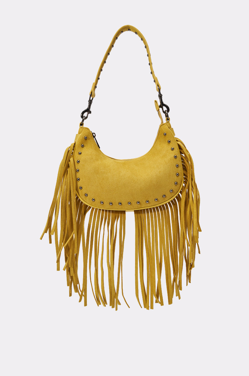 The MATCH IT BACK PURSE is a yellow boho fringe bag in soft faux suede with a curved shape, metal studs, and long fringe. It has a matching studded handle and an adjustable shoulder strap for versatile styling.