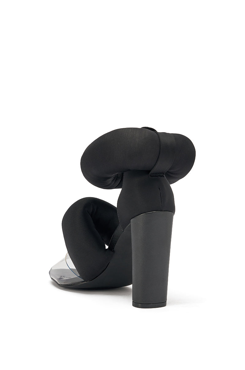 The YANIX BLACK PUFF SLIP ON SANDAL features a black chunky heel, clear front strap, and puffy straps forming bold loops at the ankle and foot, with an open almond toe. Displayed against a plain white background. 5