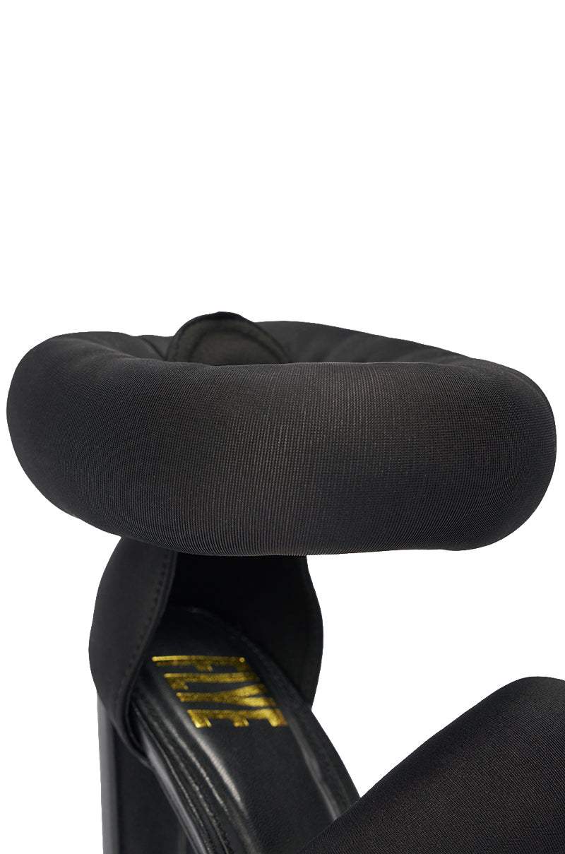 Close-up of a black cushioned strap on the YANIX BLACK PUFF SLIP ON SANDAL, with puffy details and part of a yellow logo visible below. 6