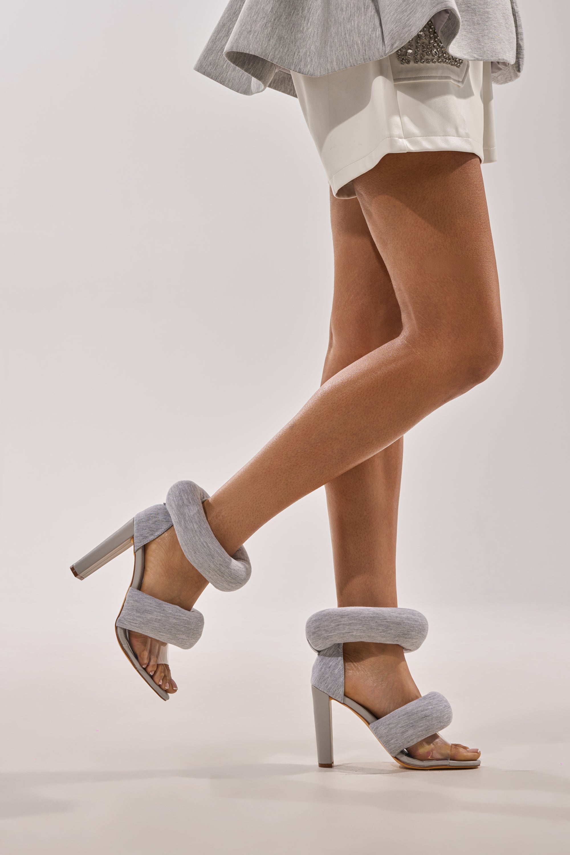 A person wearing YANIX GREY PUFF SLIP ON SANDAL with thick gray straps and white shorts stands tiptoe, one leg bent, against a light background. 2