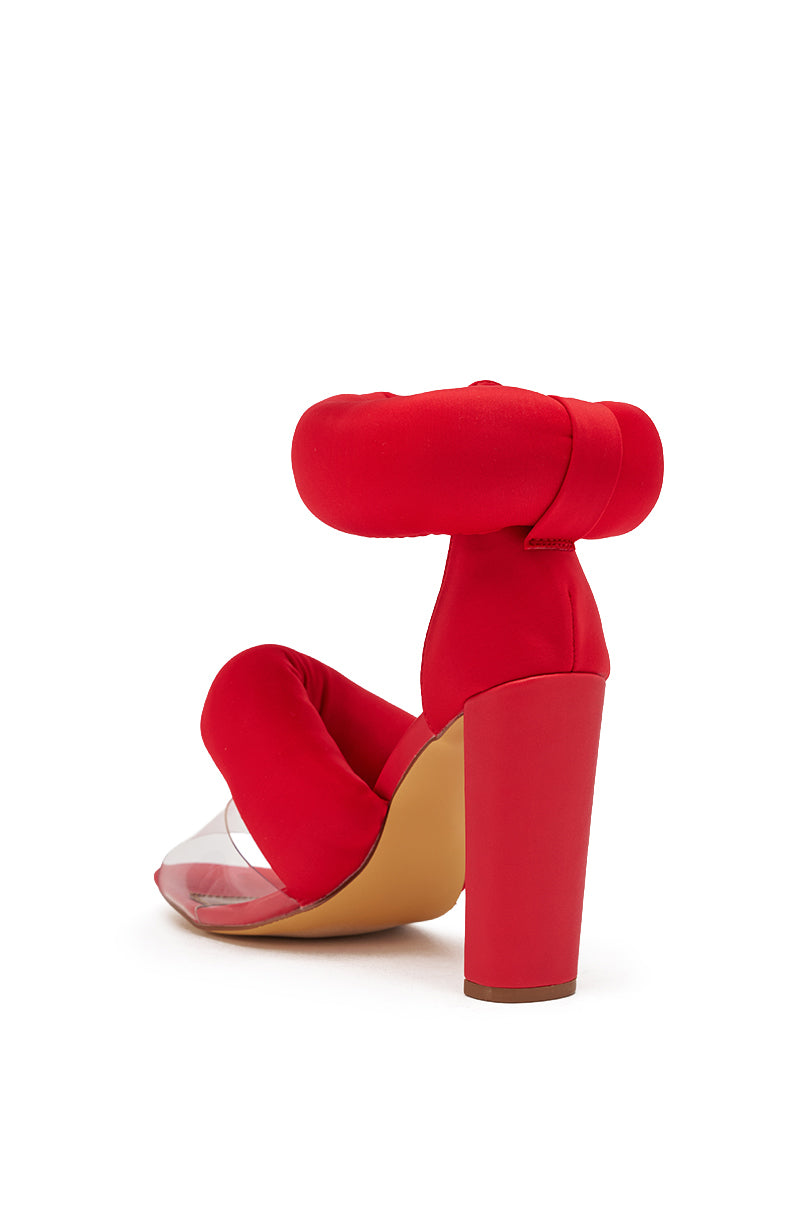 The YANIX RED PUFF SLIP ON SANDAL features a red chunky heel, cushioned puffy ankle and toe straps, and a clear vinyl front section, shown against a white background. 5