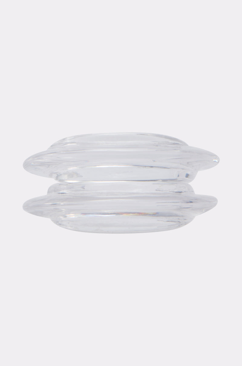 The ARTISTIC STATEMENT BRACELET is a clear, round glass accessory featuring two wide, flat parallel discs linked by a slim central section, exuding a refined minimalist look, set against a light grey background.