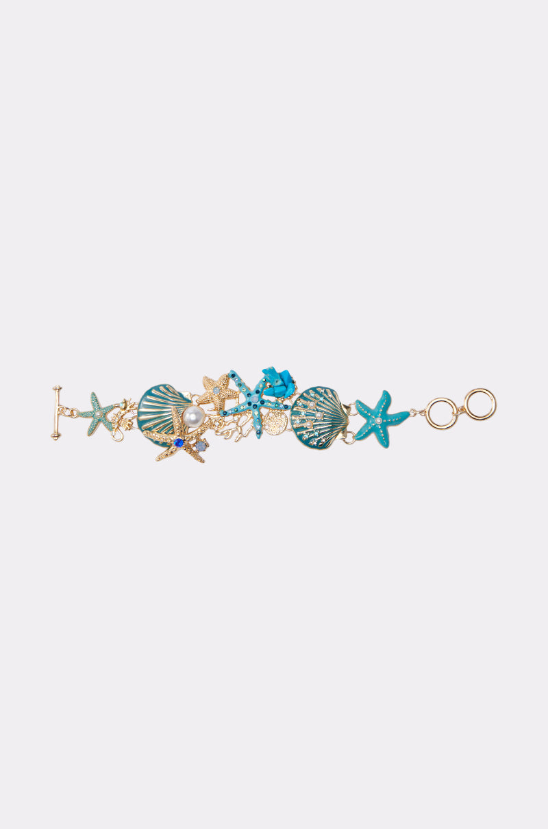 TO THE SHORE BRACELET: A gold bracelet featuring turquoise starfish, seashells, and shimmering gems for an ocean-inspired look. Sea creature motifs and a toggle clasp complete the design, shown on a light background.