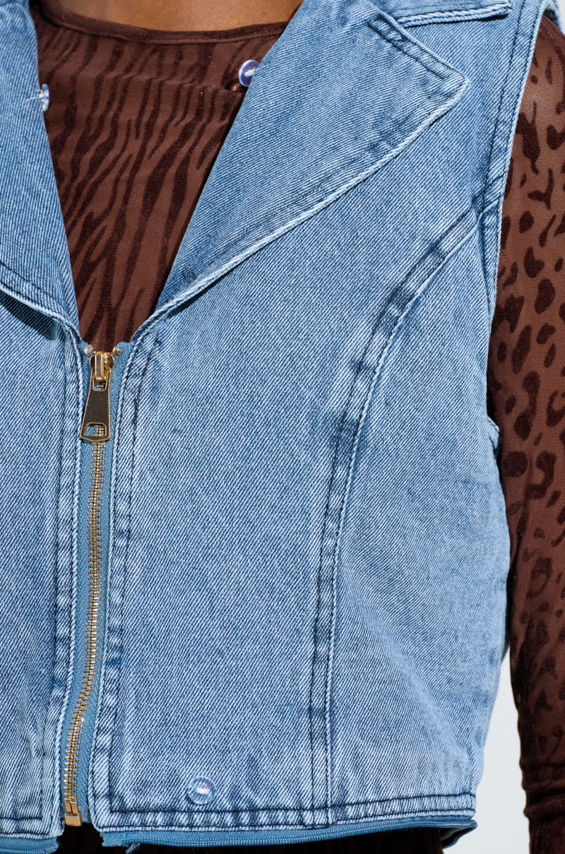 A close-up view of a person wearing the ALICIA FUR TRIM DENIM VEST over a brown, printed animal-patterned top. Only the torso is visible, highlighting the luxury vibes through the textures and patterns of these chic garments.