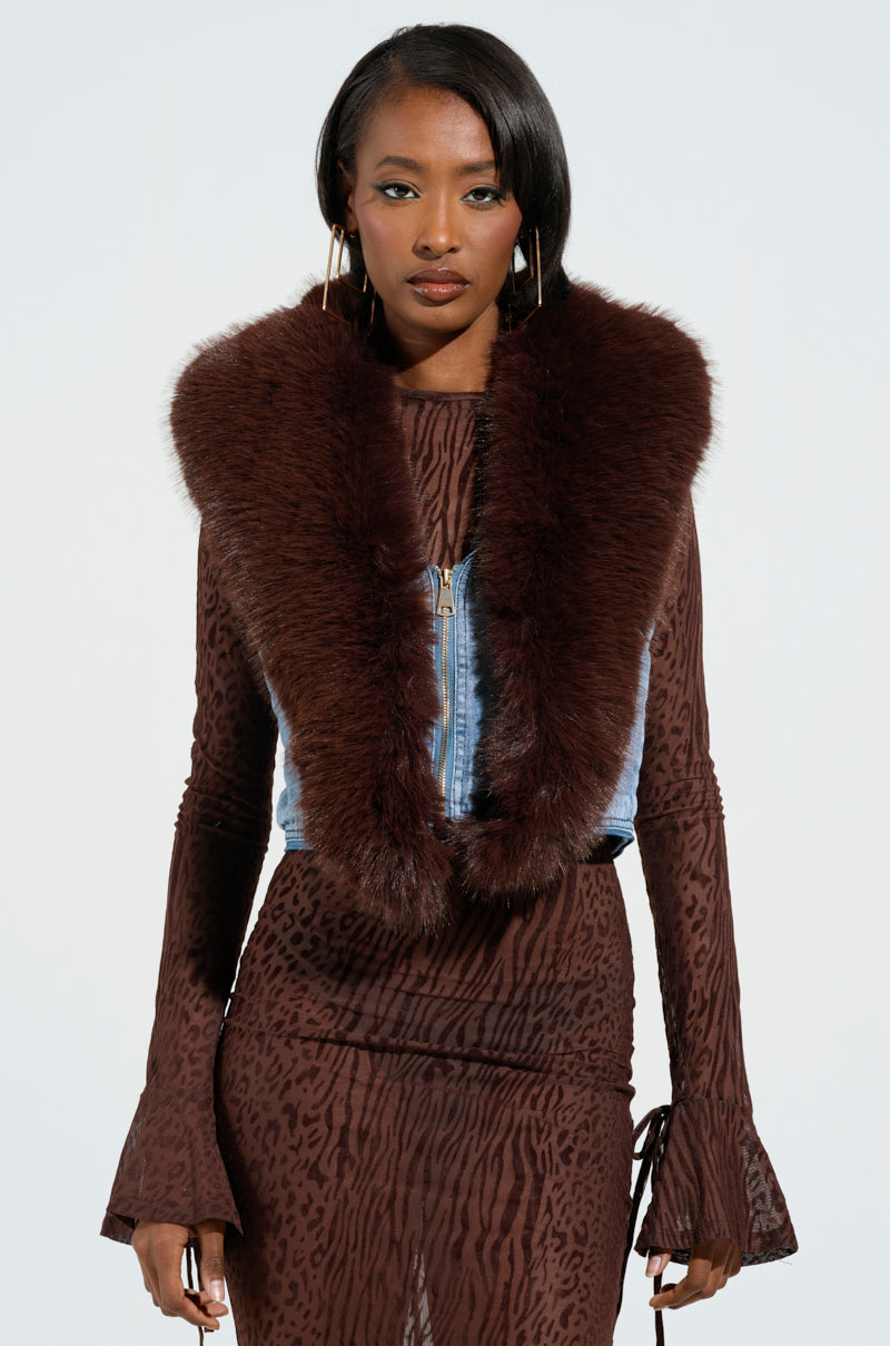 A person is flaunting a luxurious vibe in a brown, patterned outfit complemented by the ALICIA FUR TRIM DENIM VEST, distinguished by its fur-trimmed collar. The ensemble boasts long sleeves with flared cuffs and stands out beautifully against the plain white background.