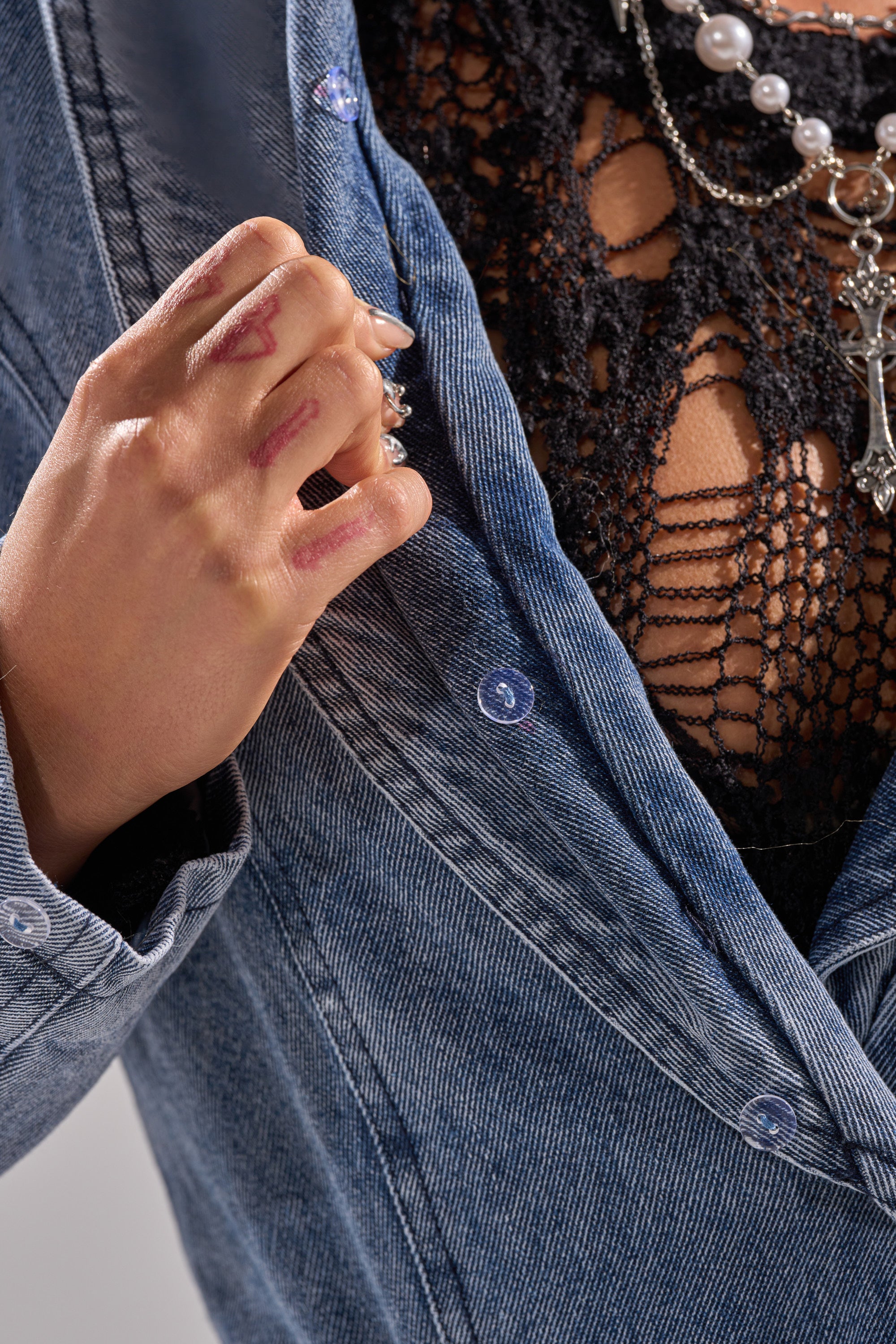 Wearing the KAYA FUR TRIM DENIM TRENCH over a black lace top and layered necklaces, she holds the jacket lapel with ink-stained fingers.