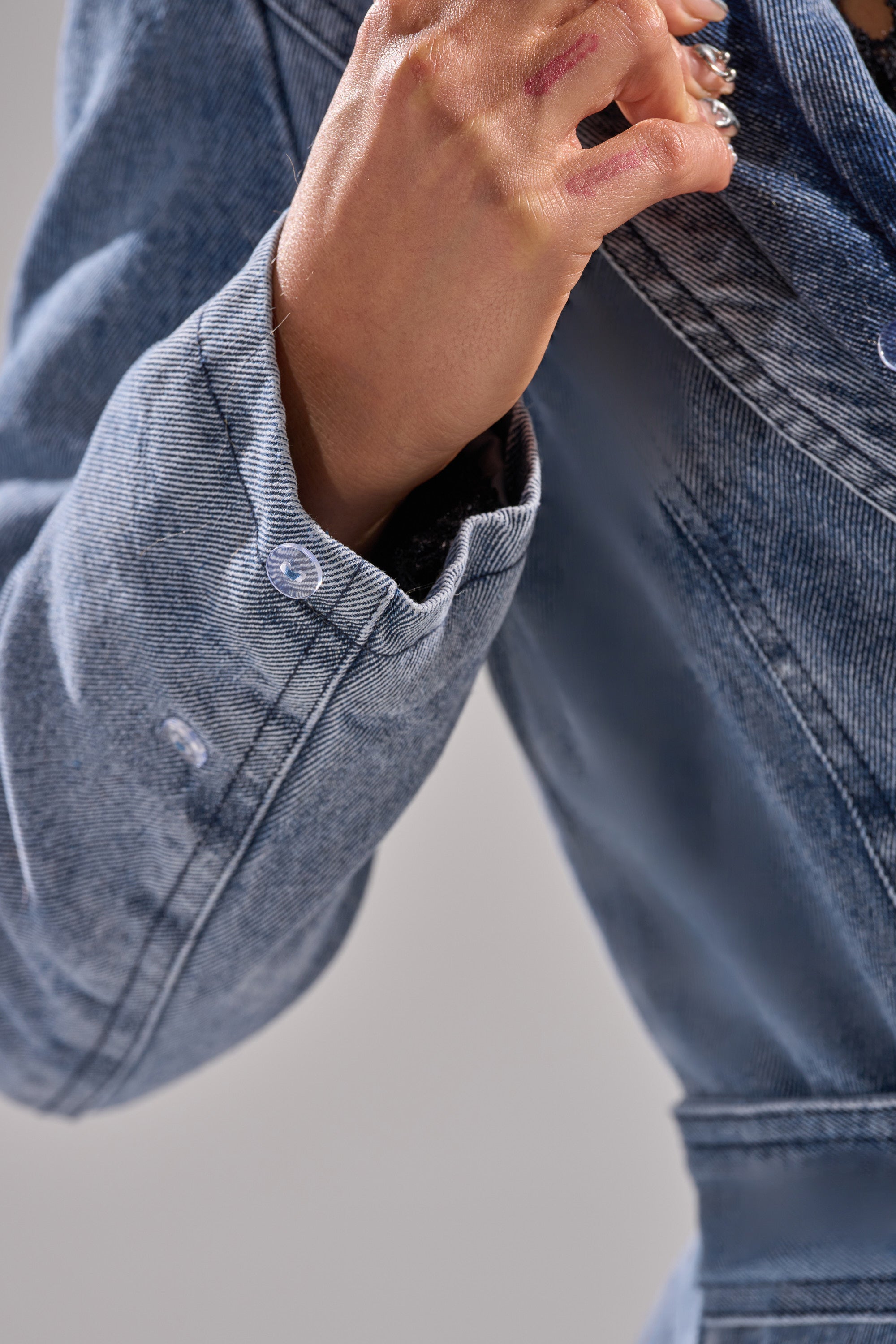 A close-up of someone wearing the KAYA FUR TRIM DENIM TRENCH, softly adjusting the collar, with a blurred, plain background.