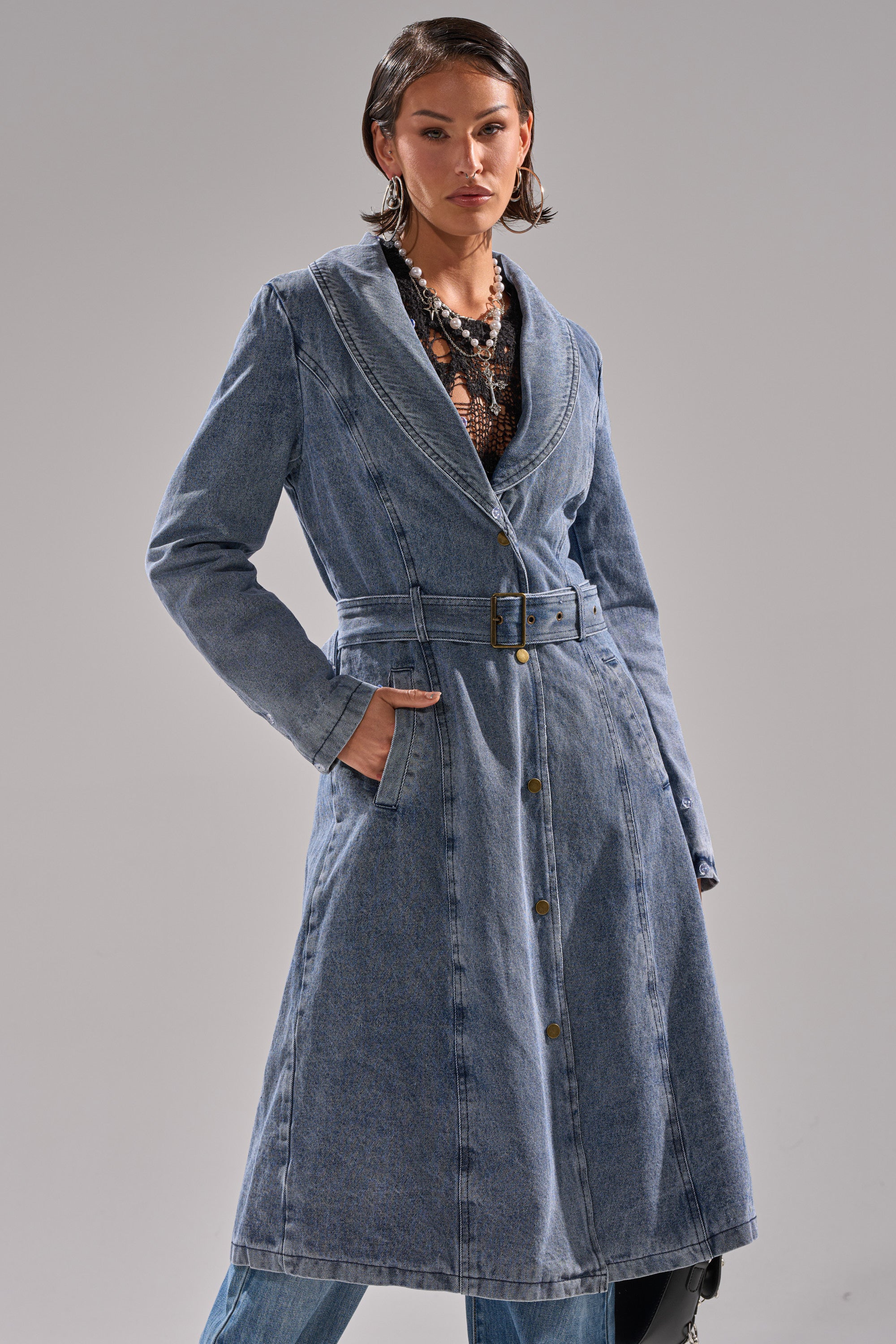 Wearing the KAYA FUR TRIM DENIM TRENCH over blue jeans and a black patterned top, a person stands against a plain background with one hand in their pocket.