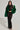 Dressed to impress, a woman exudes confidence in a black, sheer, beaded dress paired with the striking LUCKY HOODED FUR BOMBER. Her long hair cascades elegantly as she stands tall in black high-heeled sandals against a plain white background.