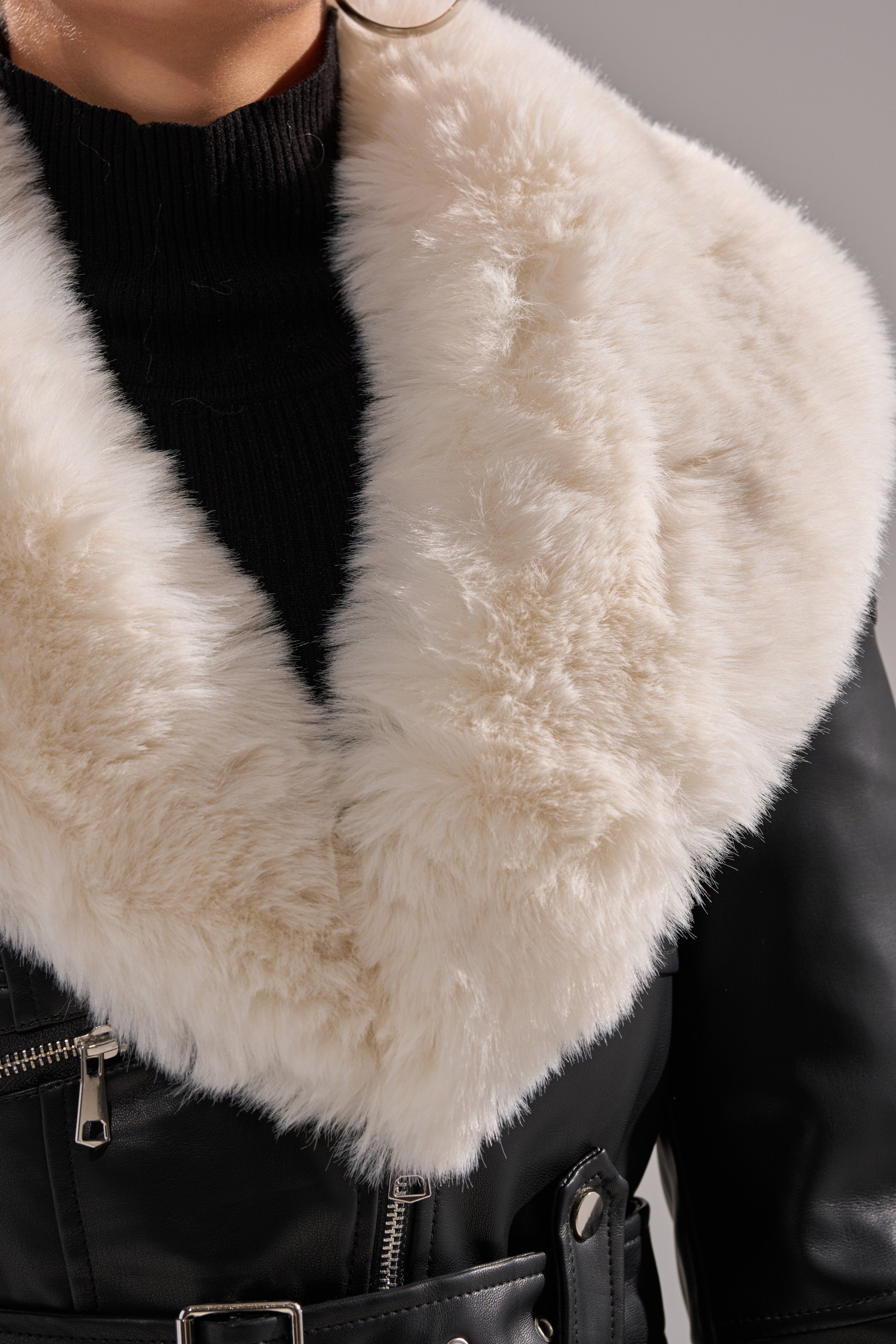 Wearing the BABY IT'S COLD OUTSIDE FUR TRIM MOTO, a person dons a black turtleneck and a moto jacket with bold white fur trim, showing only the lower half of their face and torso.