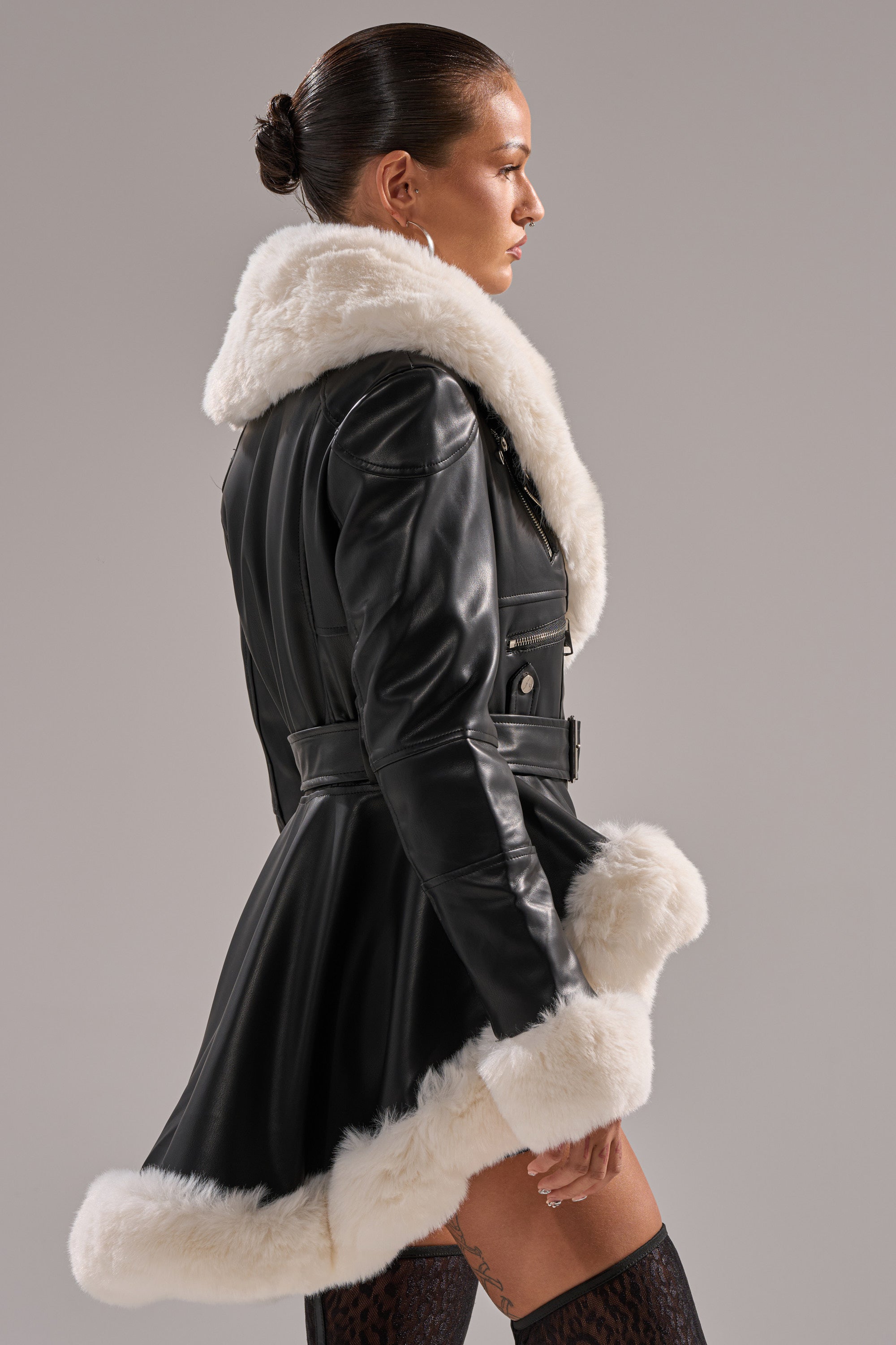 A person with slicked-back hair wears the BABY IT'S COLD OUTSIDE FUR TRIM MOTO jacket and patterned stockings. The side-profile image is set against a plain background.