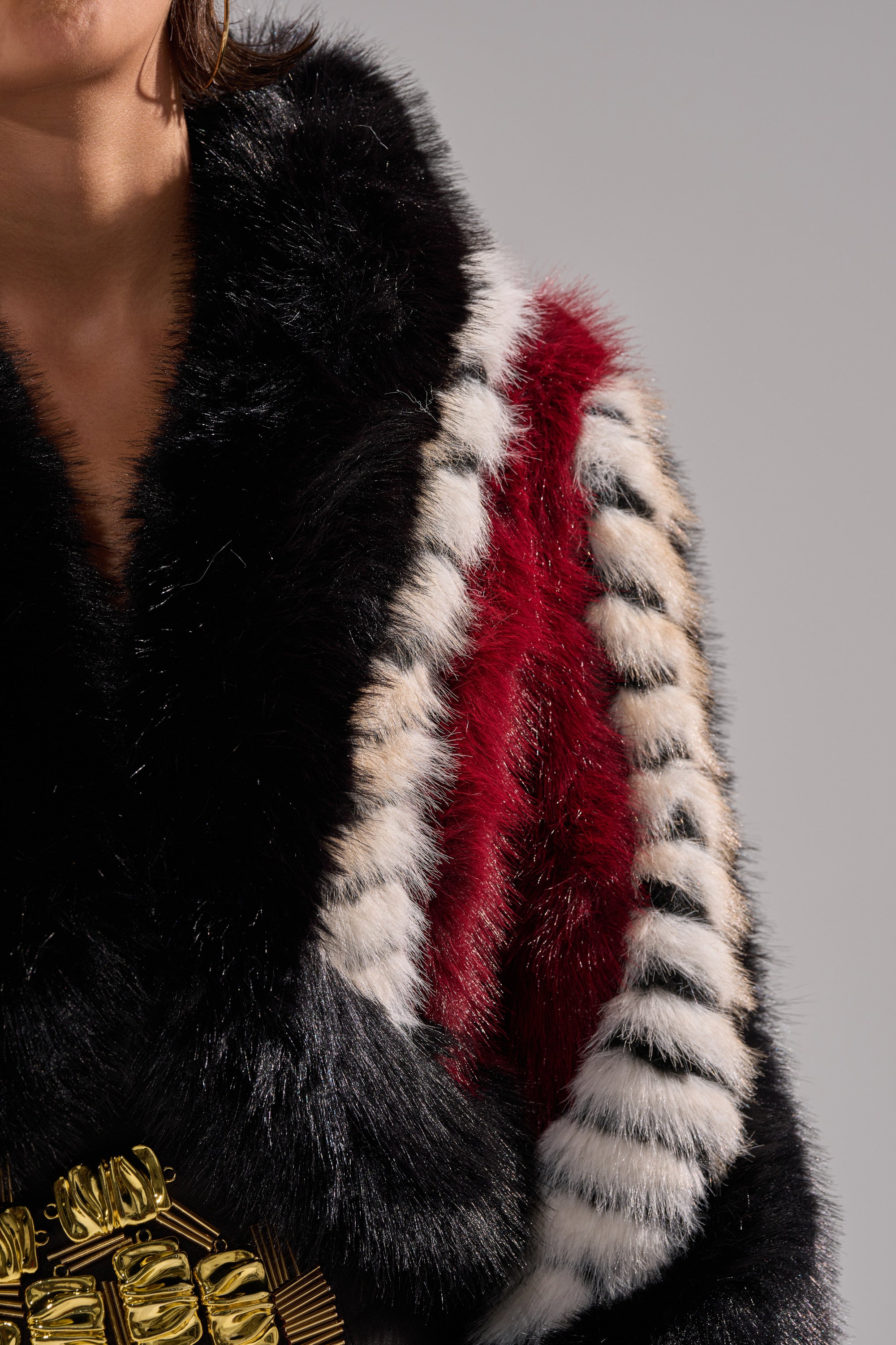 A person wears the HARD TO FIND PANELED FAUX FUR jacket featuring black, white, and red color block stripes, styled with a gold belt. The background is plain gray and the face is partially visible.