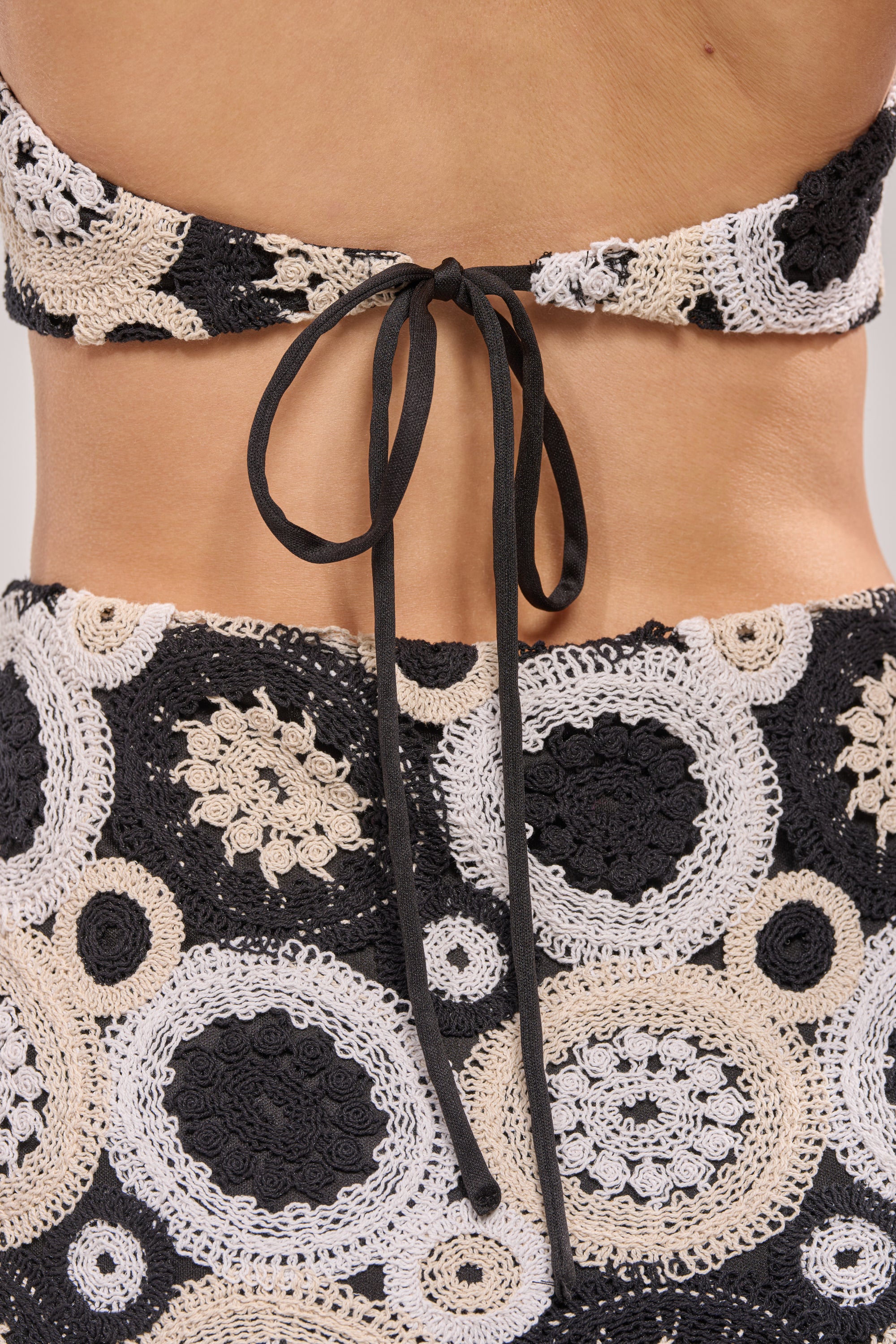 Close-up of a person's back wearing the NOT YOUR BABE CROCHET MINI DRESS IN BLACK TONAL, featuring black and white circular crochet patterns and a black string tie-back—ideal for a chic beach or festival look. 9