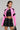 A person stands confidently in the BUBBLE POP ELECTRIC RACER MOTO jacket, paired with a sleek black faux leather crop top and a black skirt featuring lace details. Their shoulder-length hair frames their face, complemented by bold earrings and a visible tattoo on their midriff, while they hold a small black handbag.