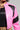 A person wearing the BUBBLE POP ELECTRIC RACER MOTO, a shiny pink and black faux leather jacket with moto-style accents, over a black top adorned with a chain necklace. The focus is on the upper body, highlighting the jacket's dynamic design and texture.