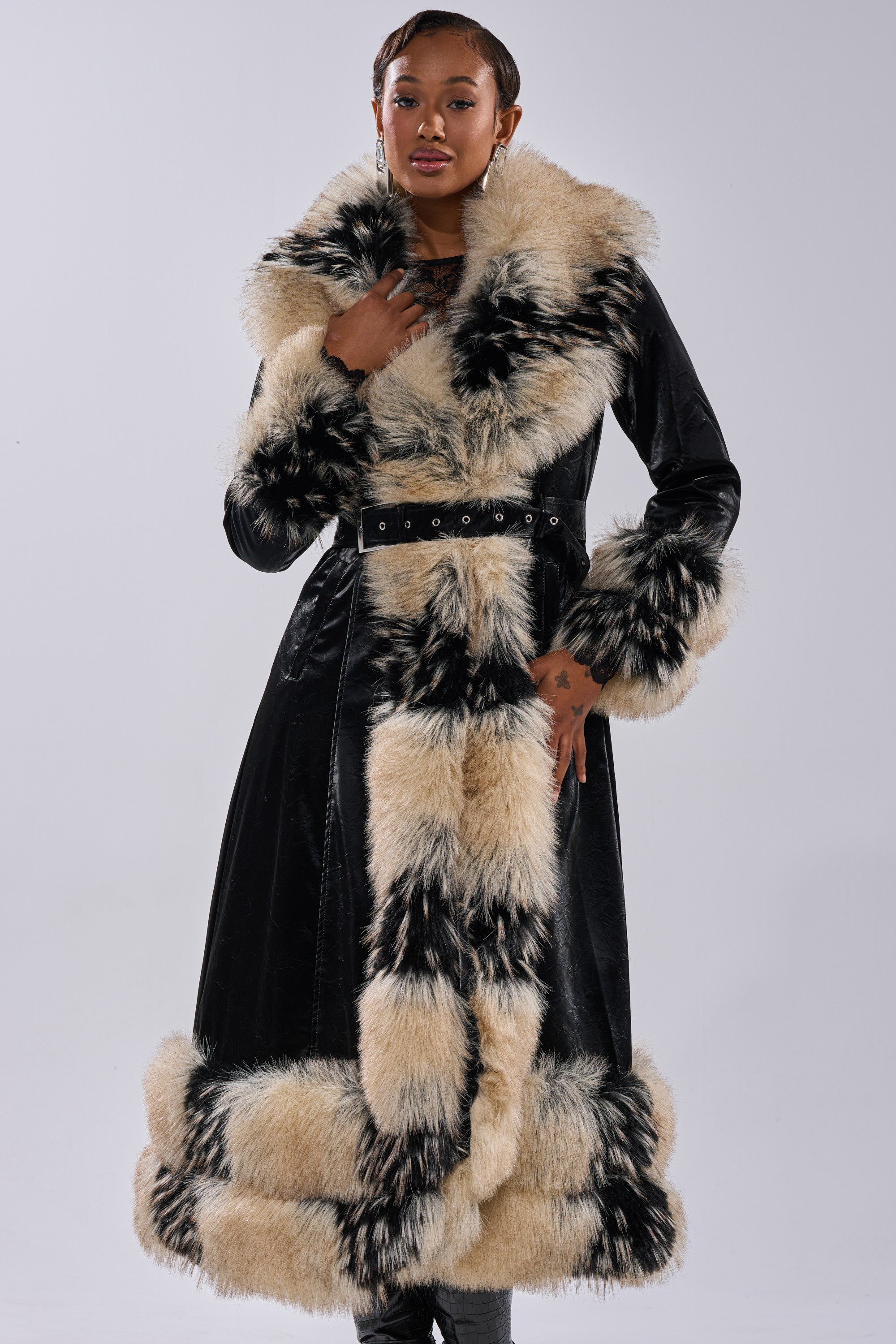 Someone poses in the VIVIAN FUR TRIM TRENCH IN LIQUID VELVET, featuring thick beige and black fur on the collar, cuffs, front, and hem, set against a plain light background.