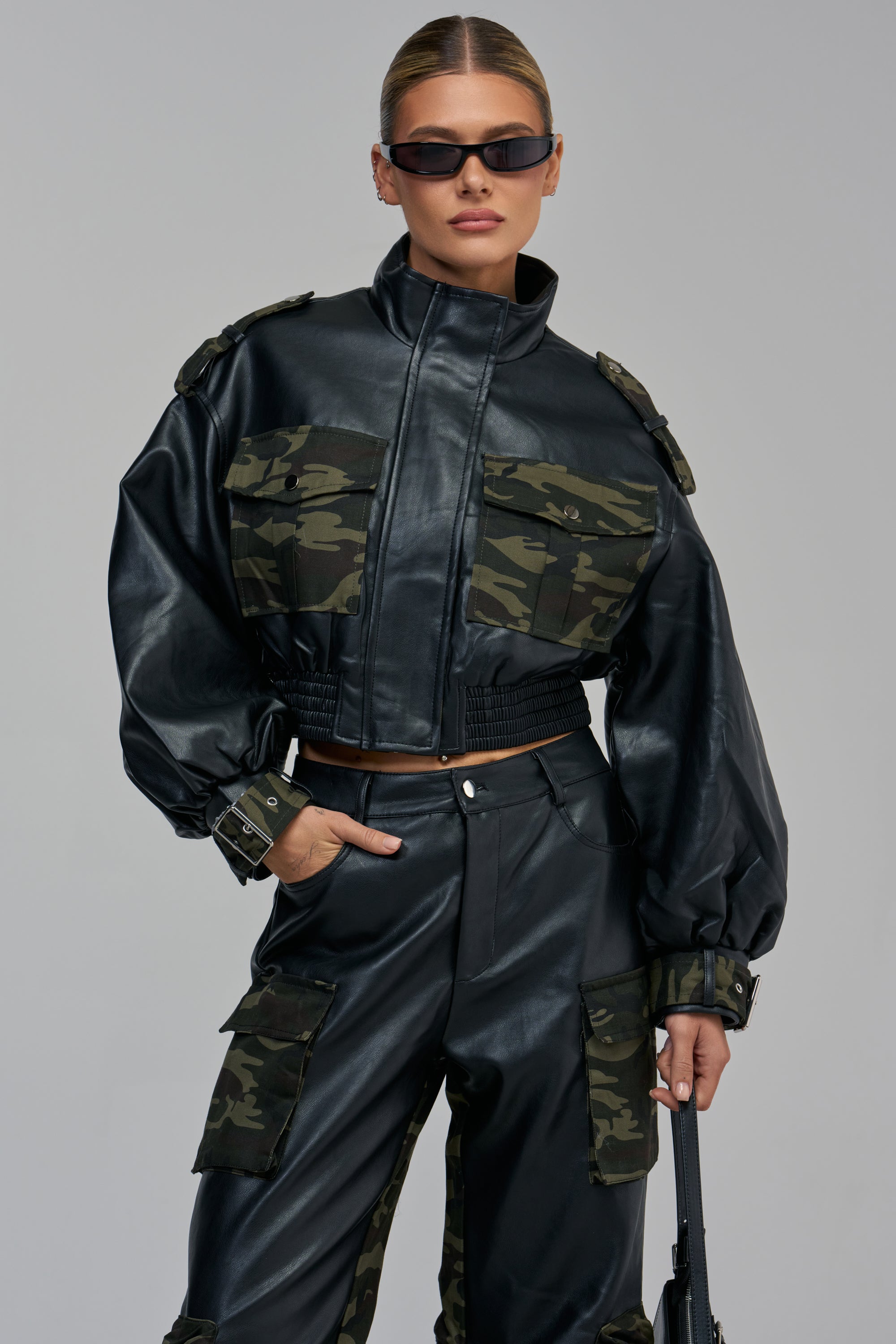 DOWN AND DIRTY FAUX LEATHER CAMO CARGO BOMBER in black faux leather with camouflage-print chest pockets and sleeve cuffs, worn with matching camo-accented cargo pants for a streetwear look.