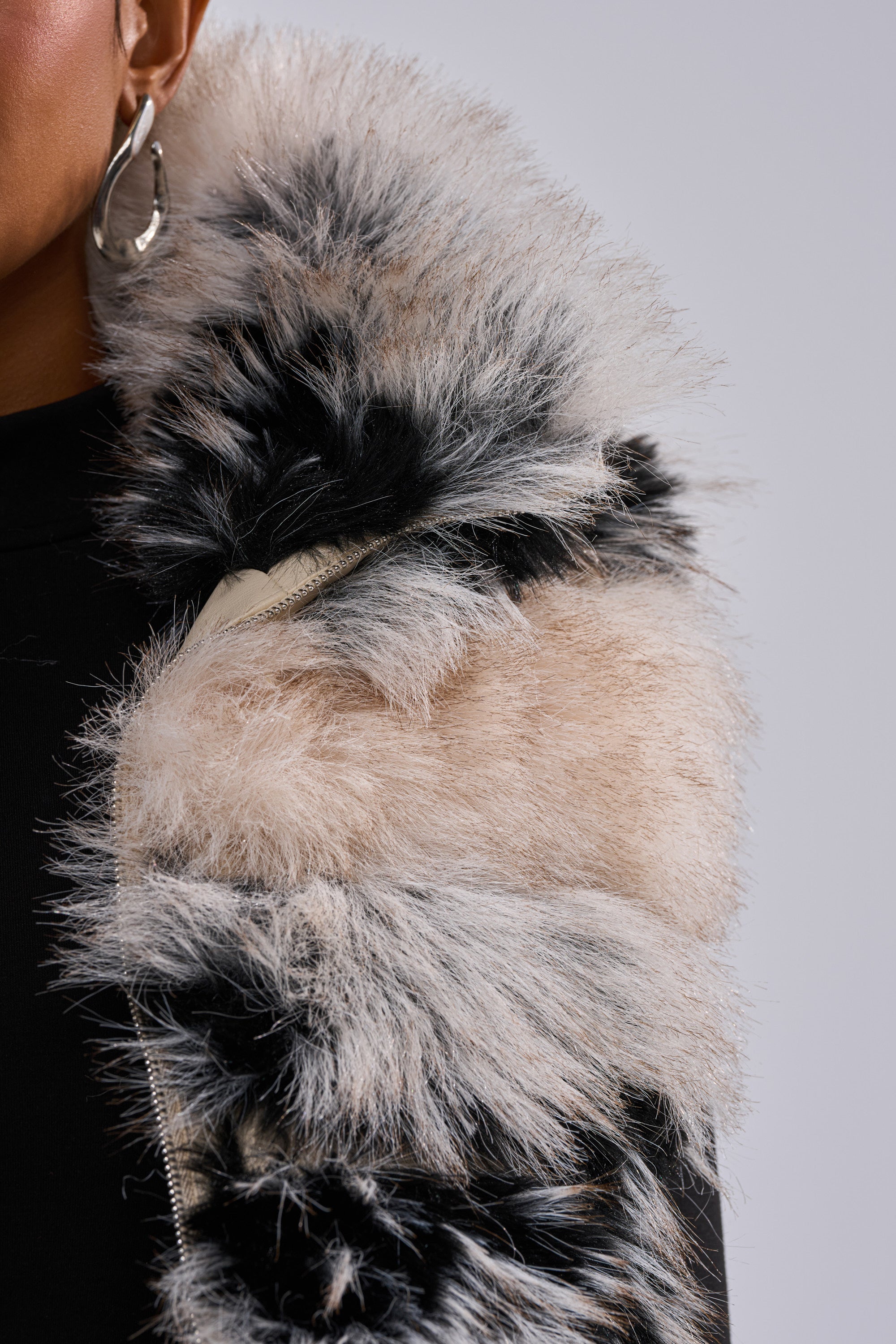 Close-up of a person wearing the KIKI FAUX FUR VEST, featuring cream, black, and gray tones in a striped two-tone design. They accessorize with a large silver hoop earring; only part of their face and upper body is visible.