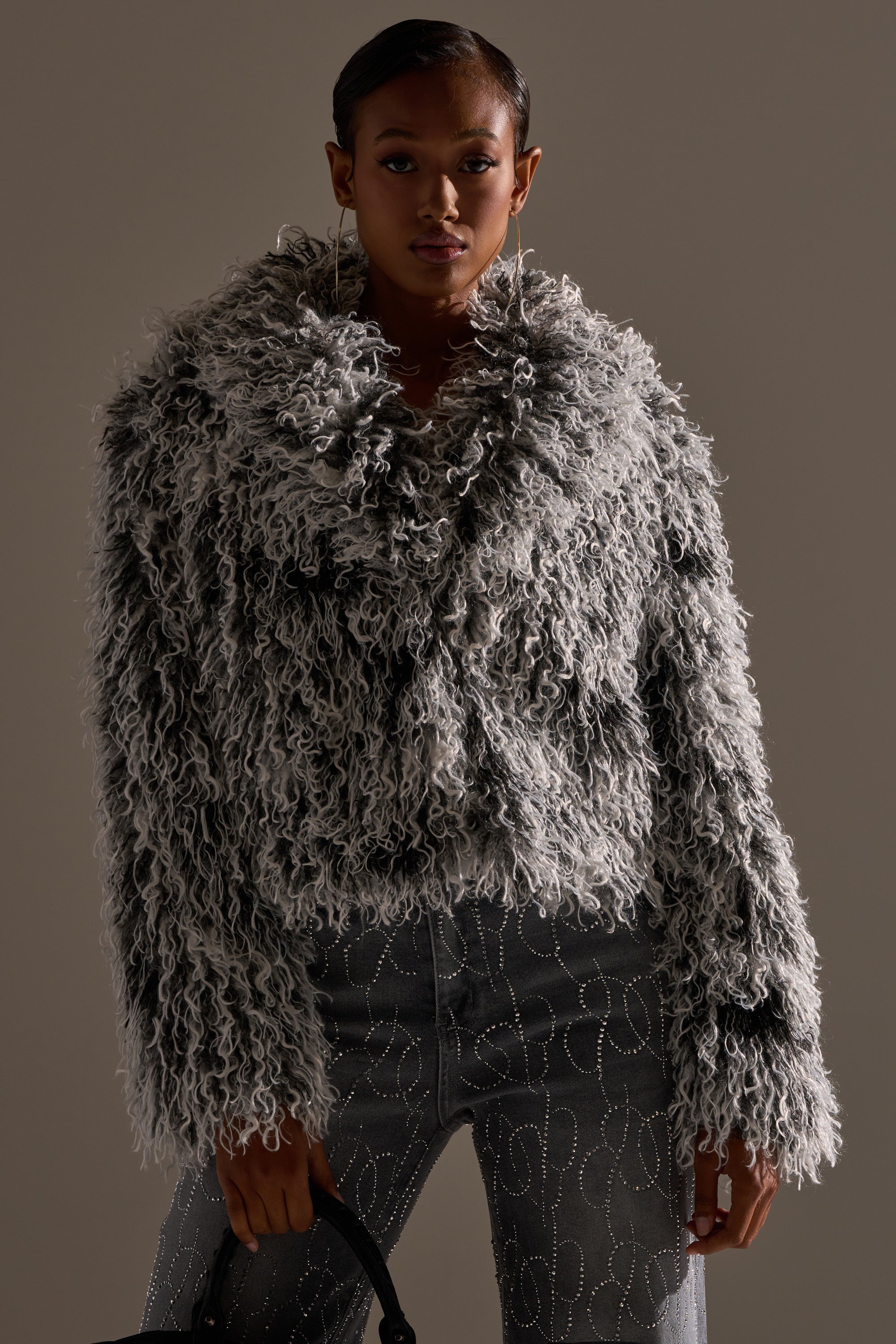 Wearing the RENDEZVOUS SHAGGY FAUX FUR coat in textured gray, paired with gray swirl-patterned jeans and a black handbag, the person poses against a neutral background.