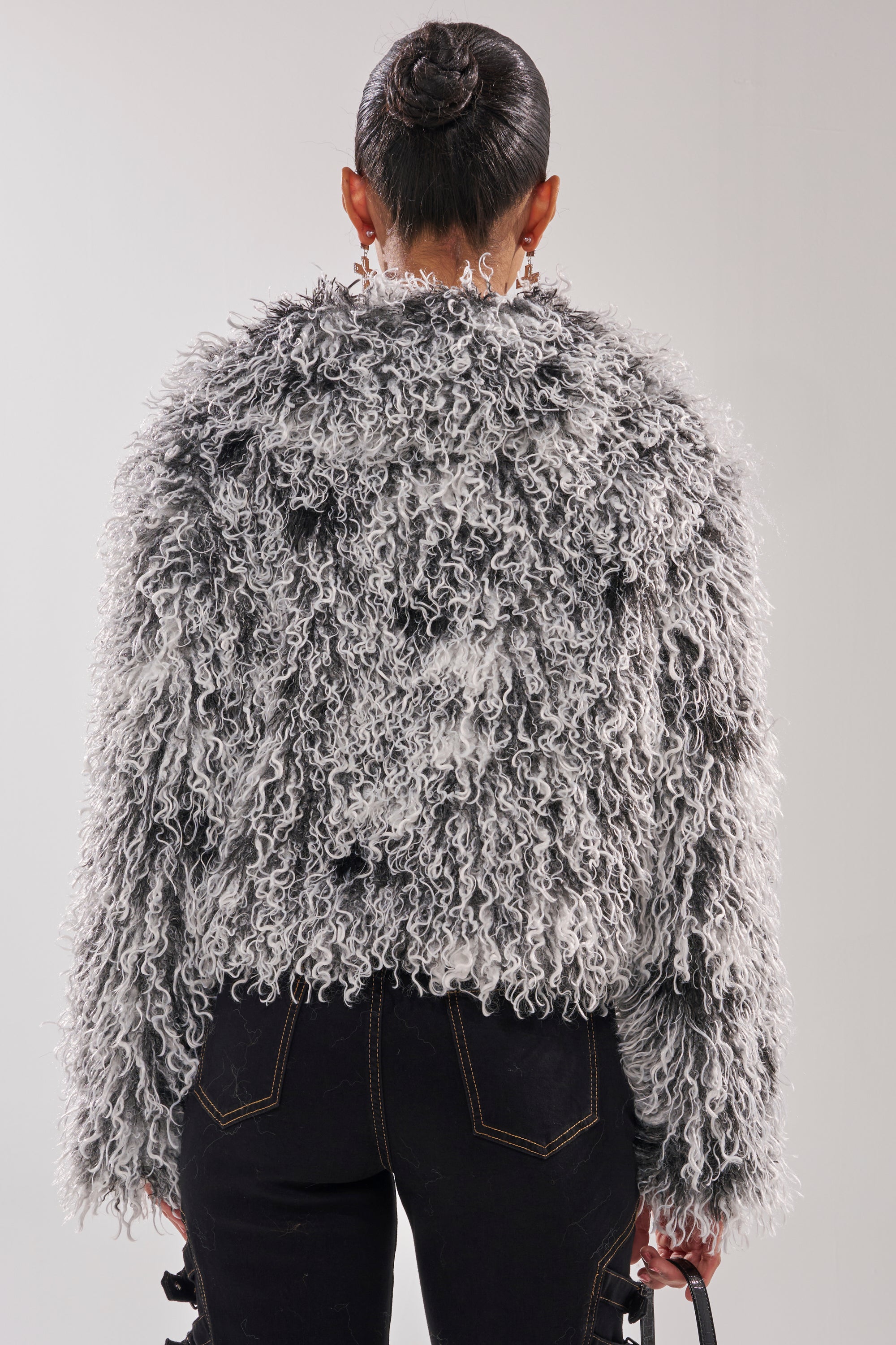A person with hair in a neat bun is seen from behind, wearing RENDEZVOUS SHAGGY FAUX FUR in textured, curly gray and black, paired with black pants and holding a small handbag. 4