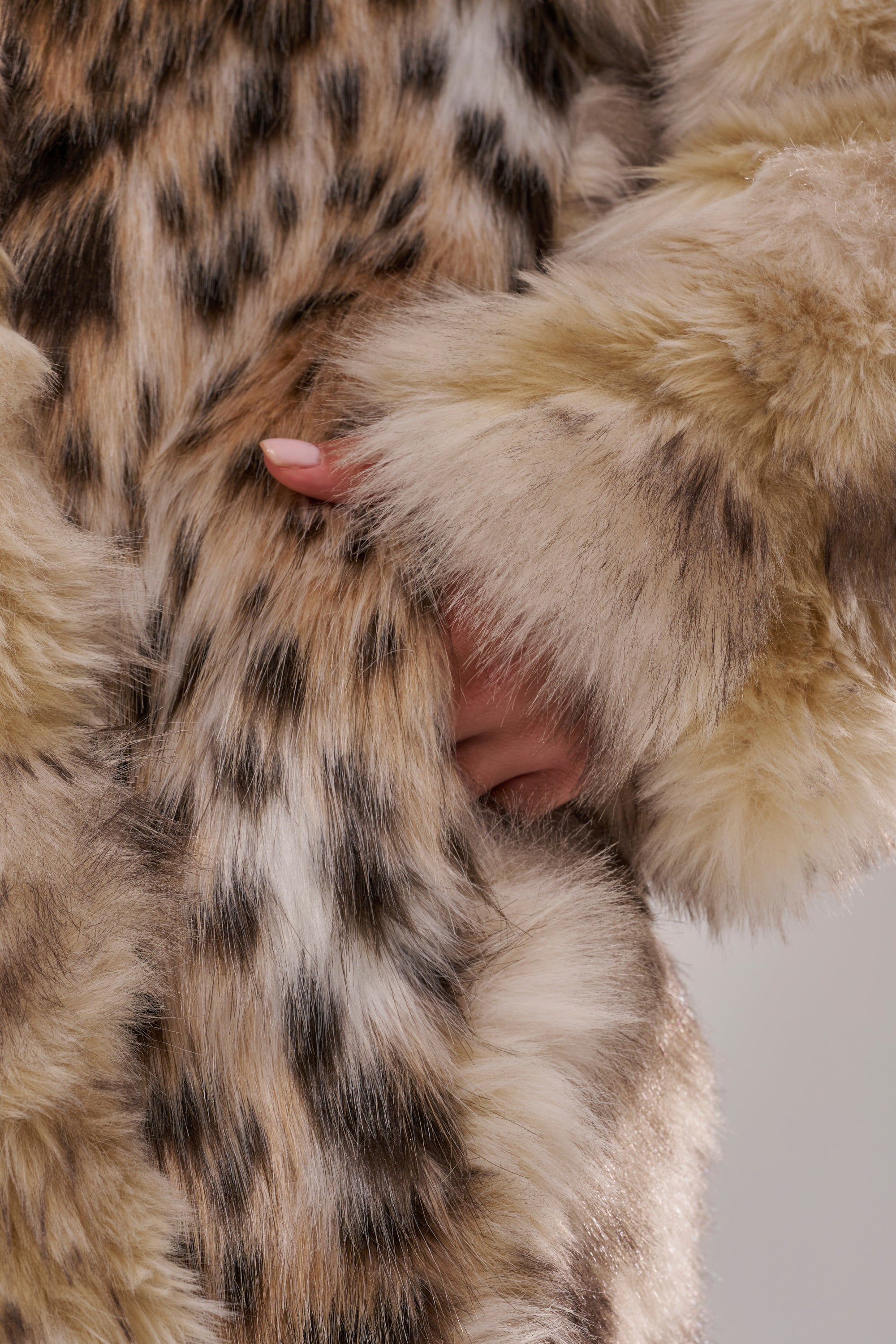 A close-up of a hand in the pocket of the PARK AVENUE PATCHWORK FAUX FUR coat, featuring fluffy faux fur in tan, brown, and cream for a cozy patchwork look.