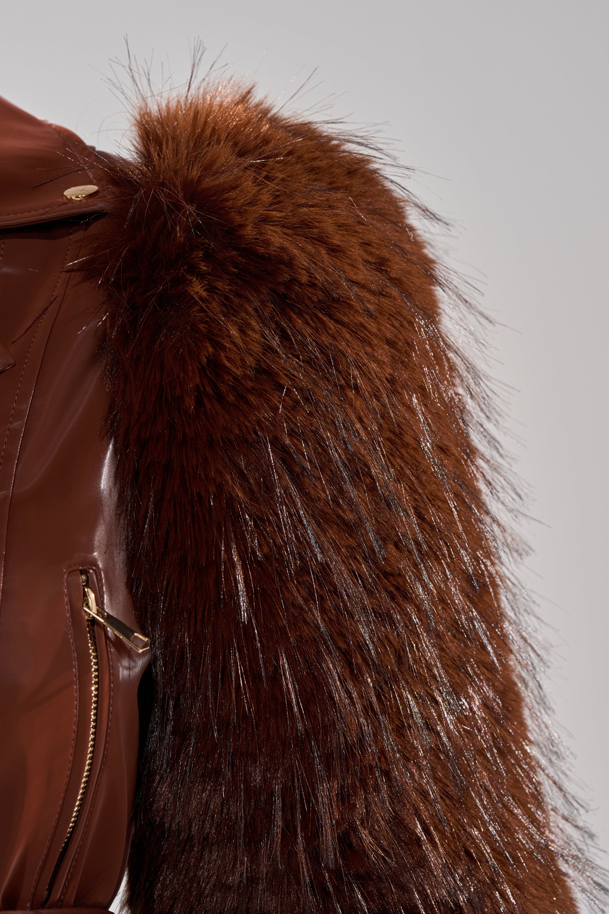 Close-up of the SPEND IT ALL FUR TRIM MOTO jacket, showcasing a shiny gold zipper and thick, dark brown faux fur sleeves. The contrasting faux leather and fur textures add striking detail to this bold, stylish piece. 13