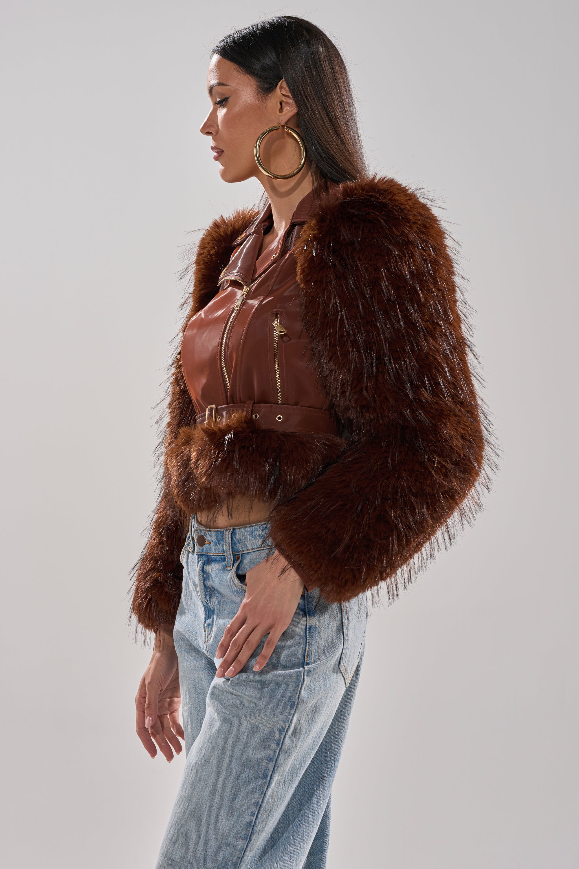 Woman in profile wears large hoop earrings, light blue jeans, and the chic SPEND IT ALL FUR TRIM MOTO brown faux leather jacket with faux fur sleeves, against a plain light background. 5