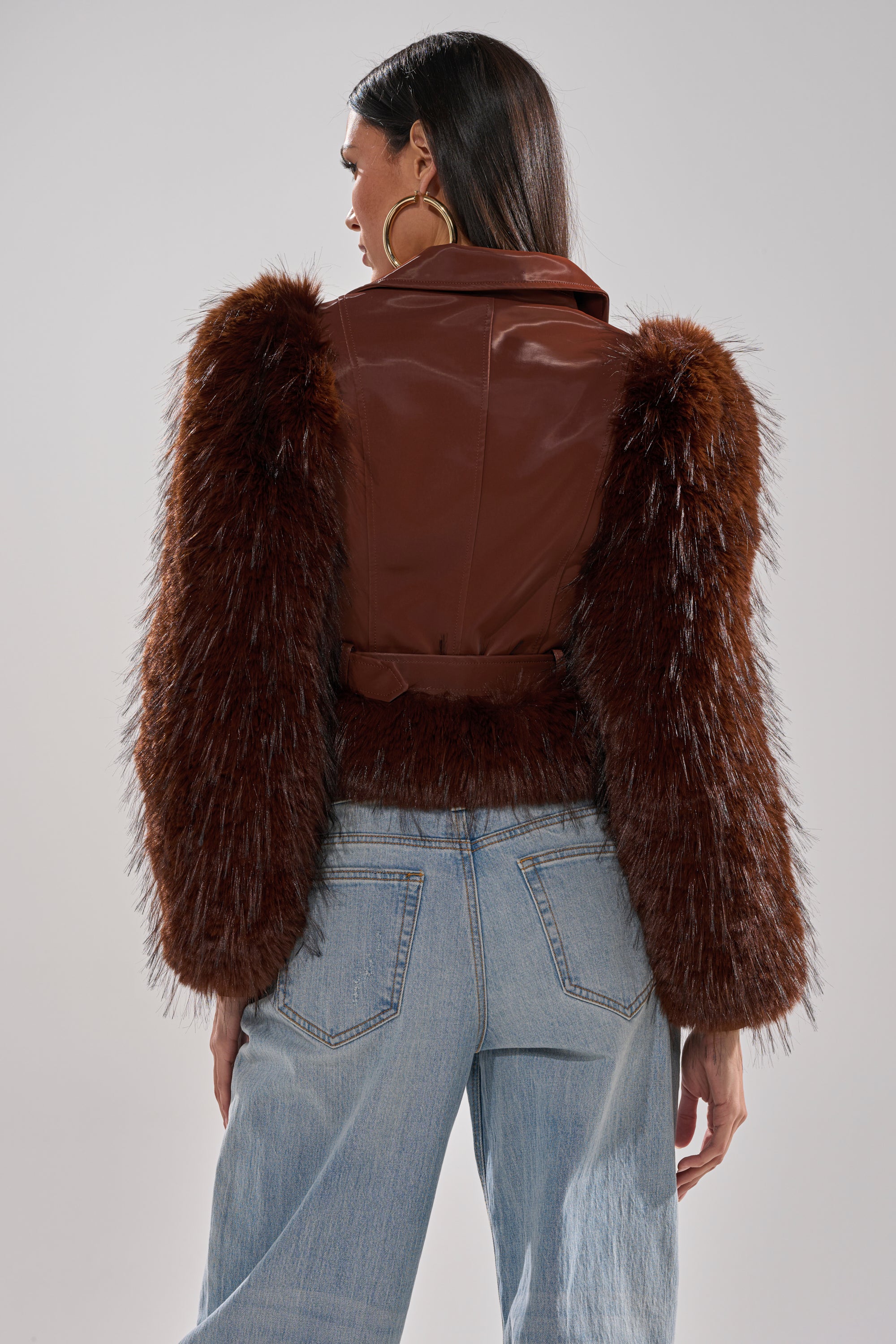 A person is shown from the back, standing against a plain gray background, wearing the SPEND IT ALL FUR TRIM MOTO jacket with shaggy faux fur sleeves and light blue jeans. 6