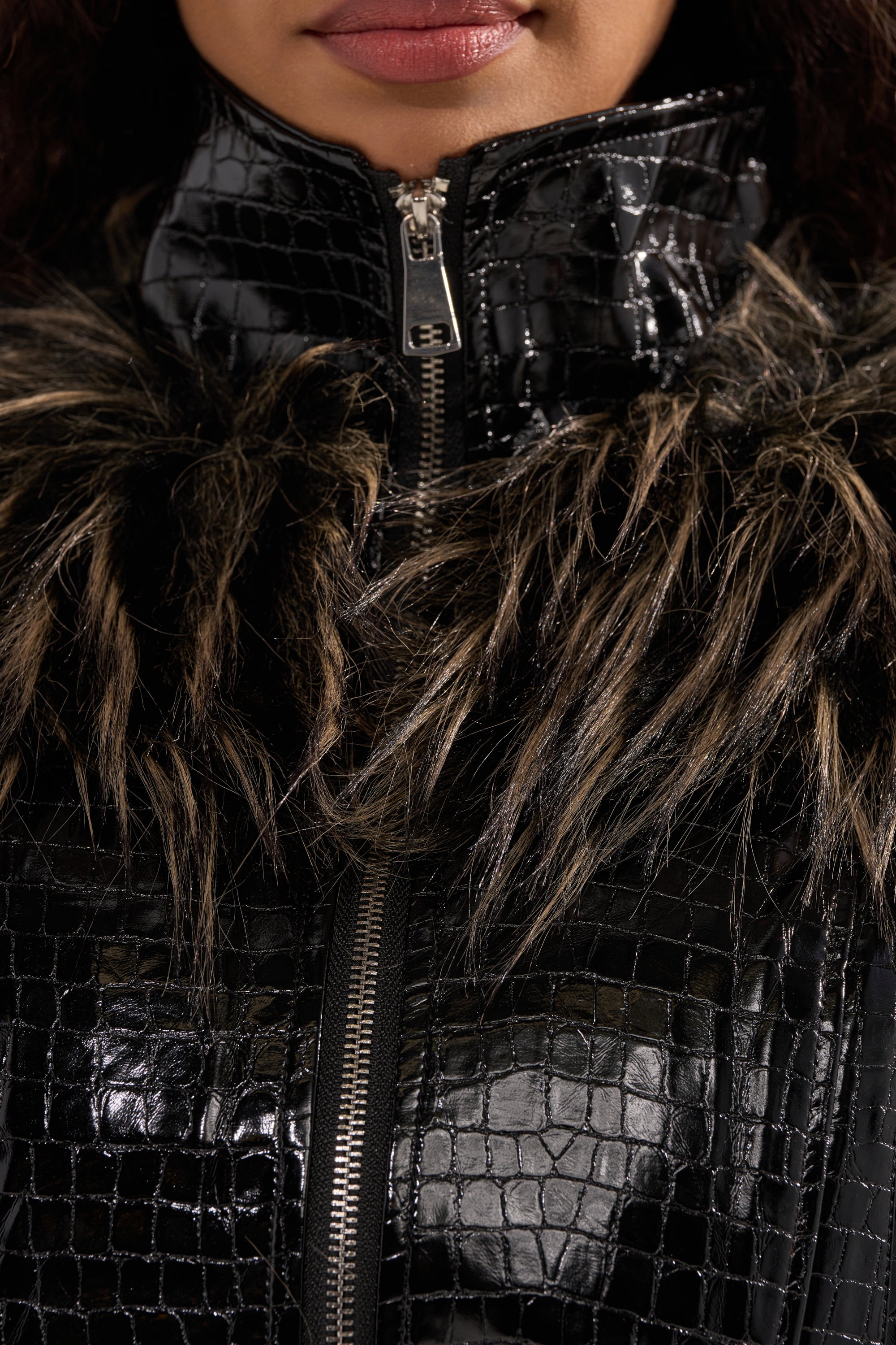 A close-up shows a person wearing the LIGHT IT UP FUR TRIM MOTO, a shiny black faux crocodile leather jacket with a zipper and faux fur collar. Only the lower half of the face and neck are visible. 8